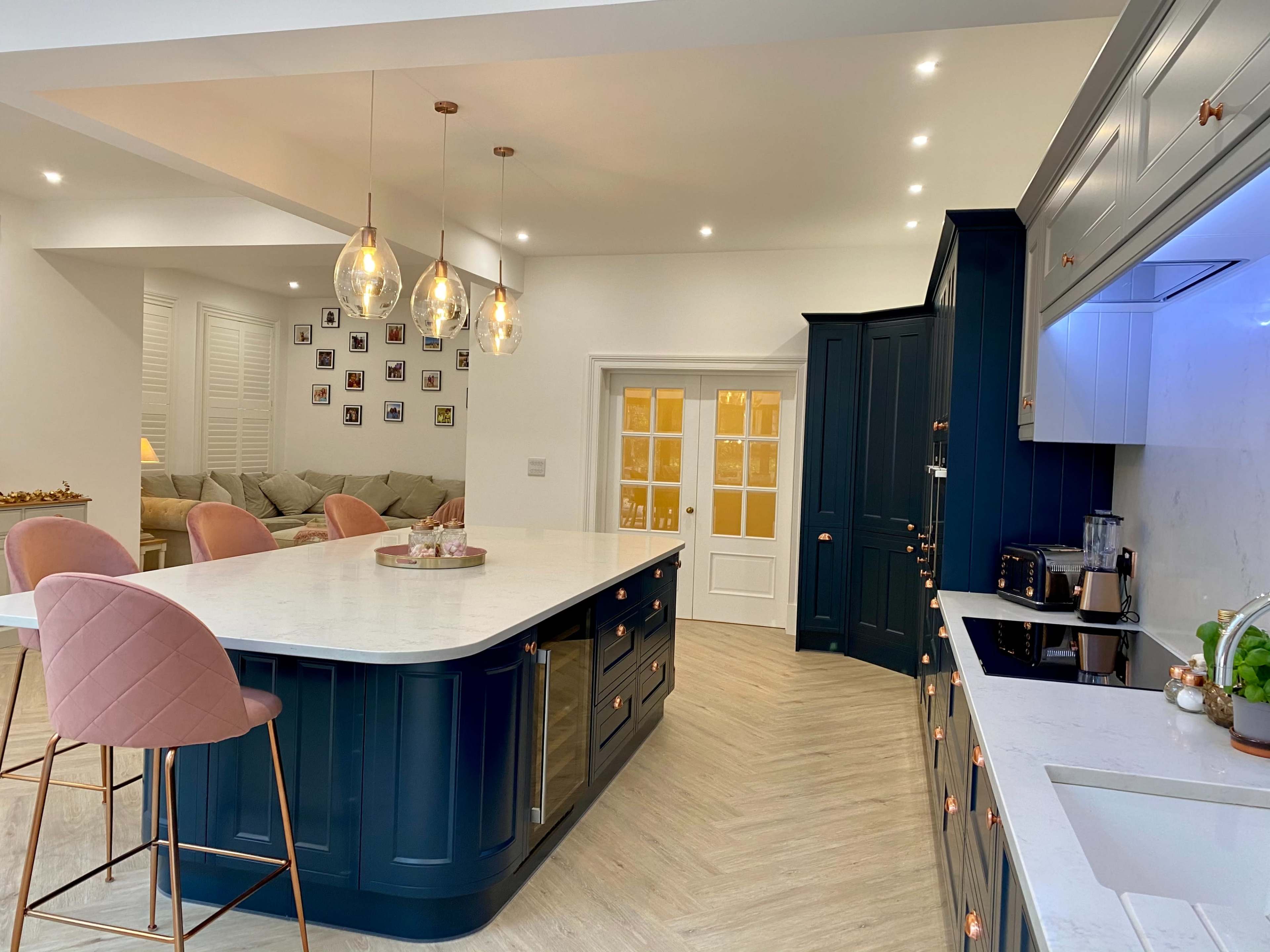 A modern kitchen with a large island, pendant lights above, and a dining area visible in the background.