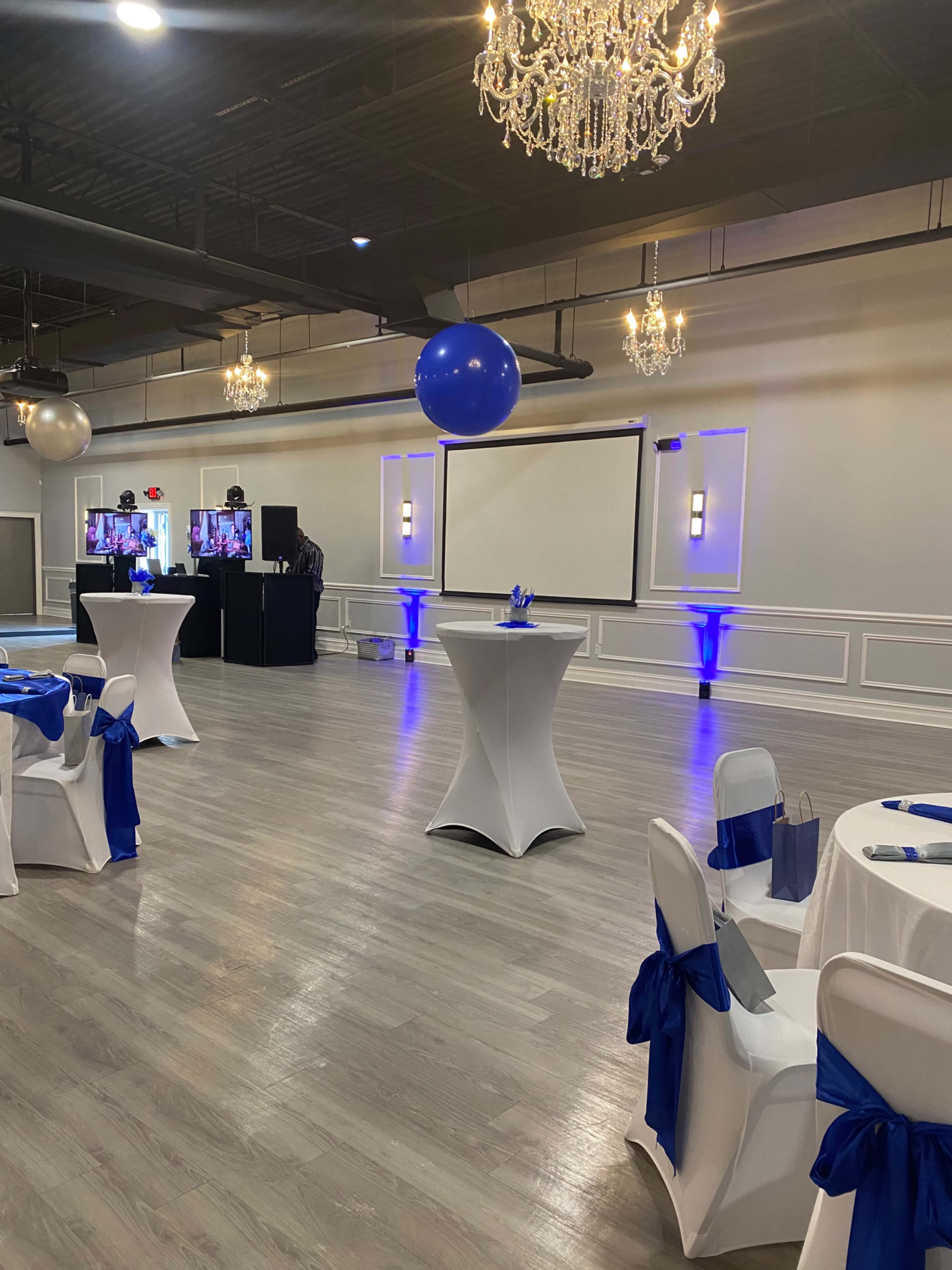 A banquet hall set up for an event, featuring tables with blue decorations and a large screen at the front.