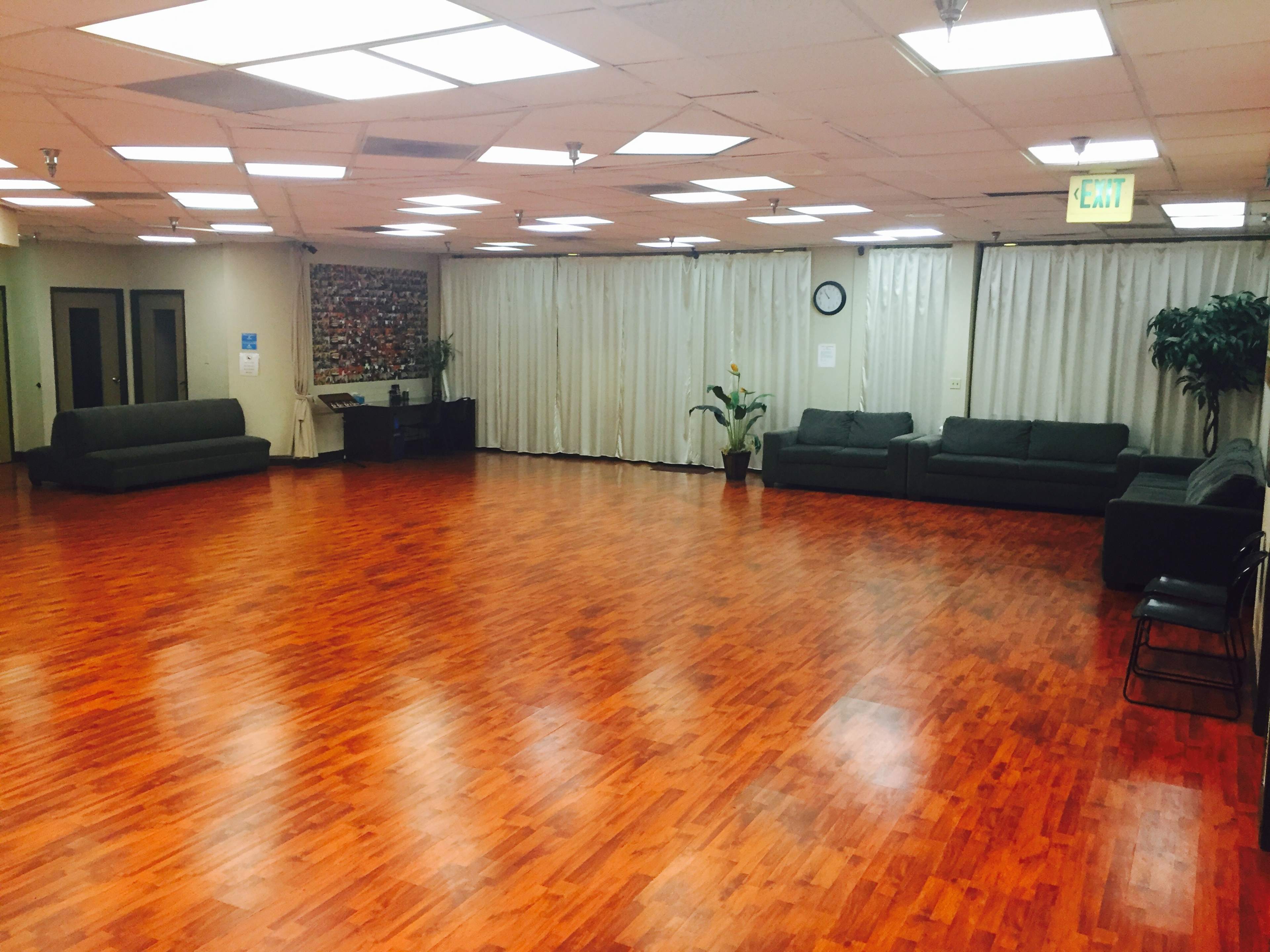 A spacious room with wooden flooring, several green couches along the walls, and bright overhead lighting.