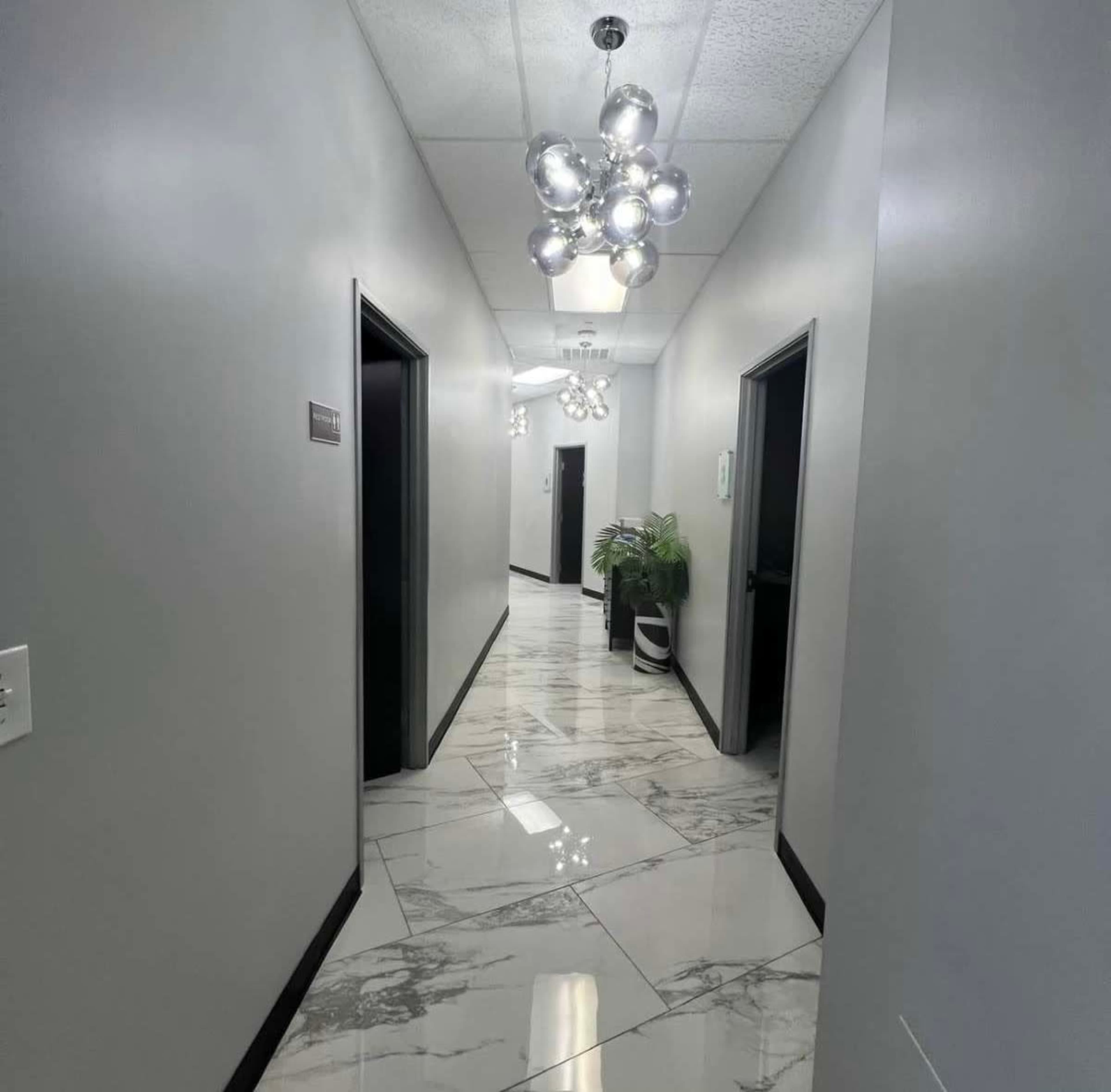 The image shows a long, well-lit hallway with glossy marble flooring and several closed doors on either side.