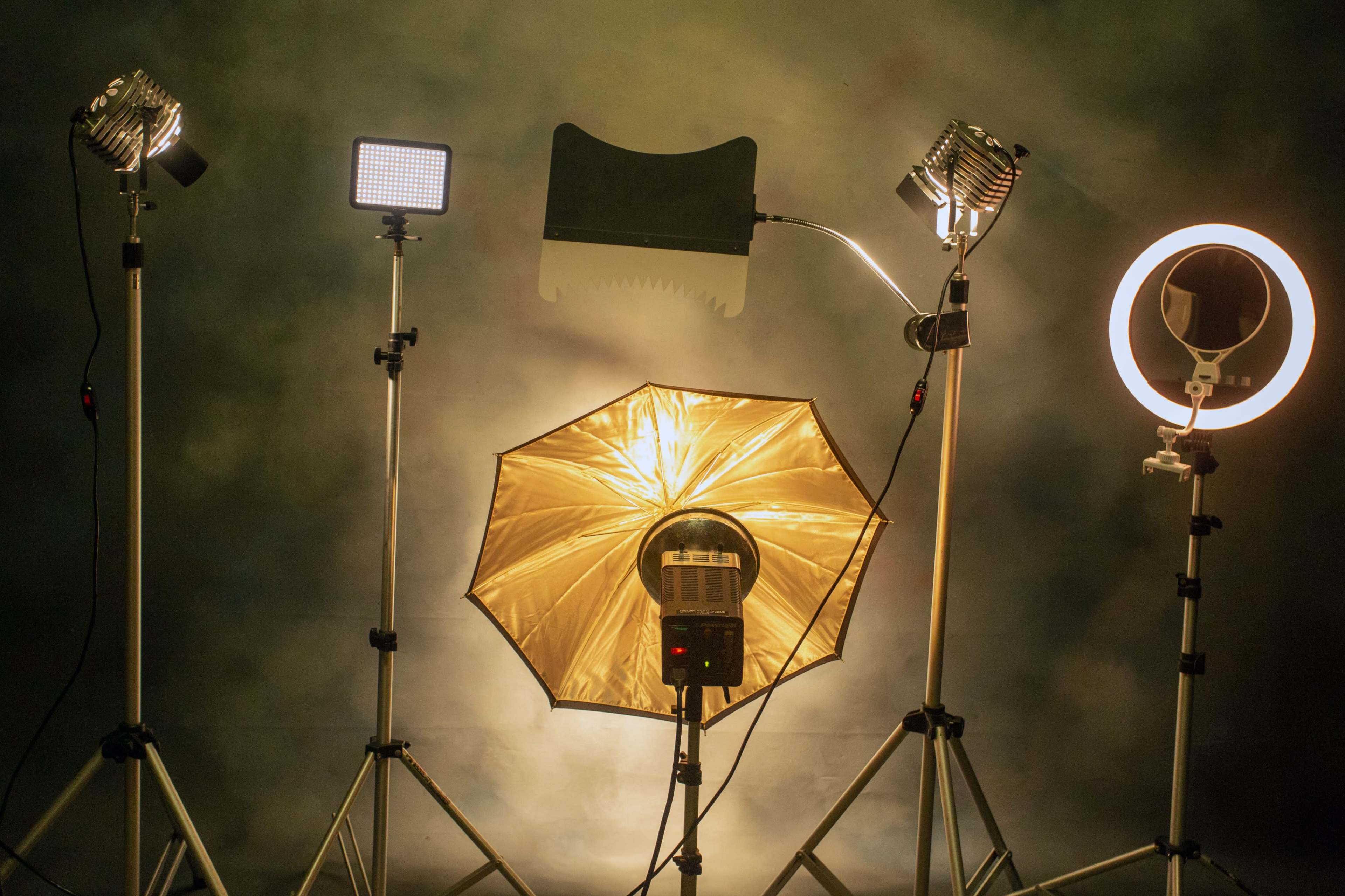 A setup of various lighting equipment, including softboxes and ring lights, arranged on tripods against a backdrop.