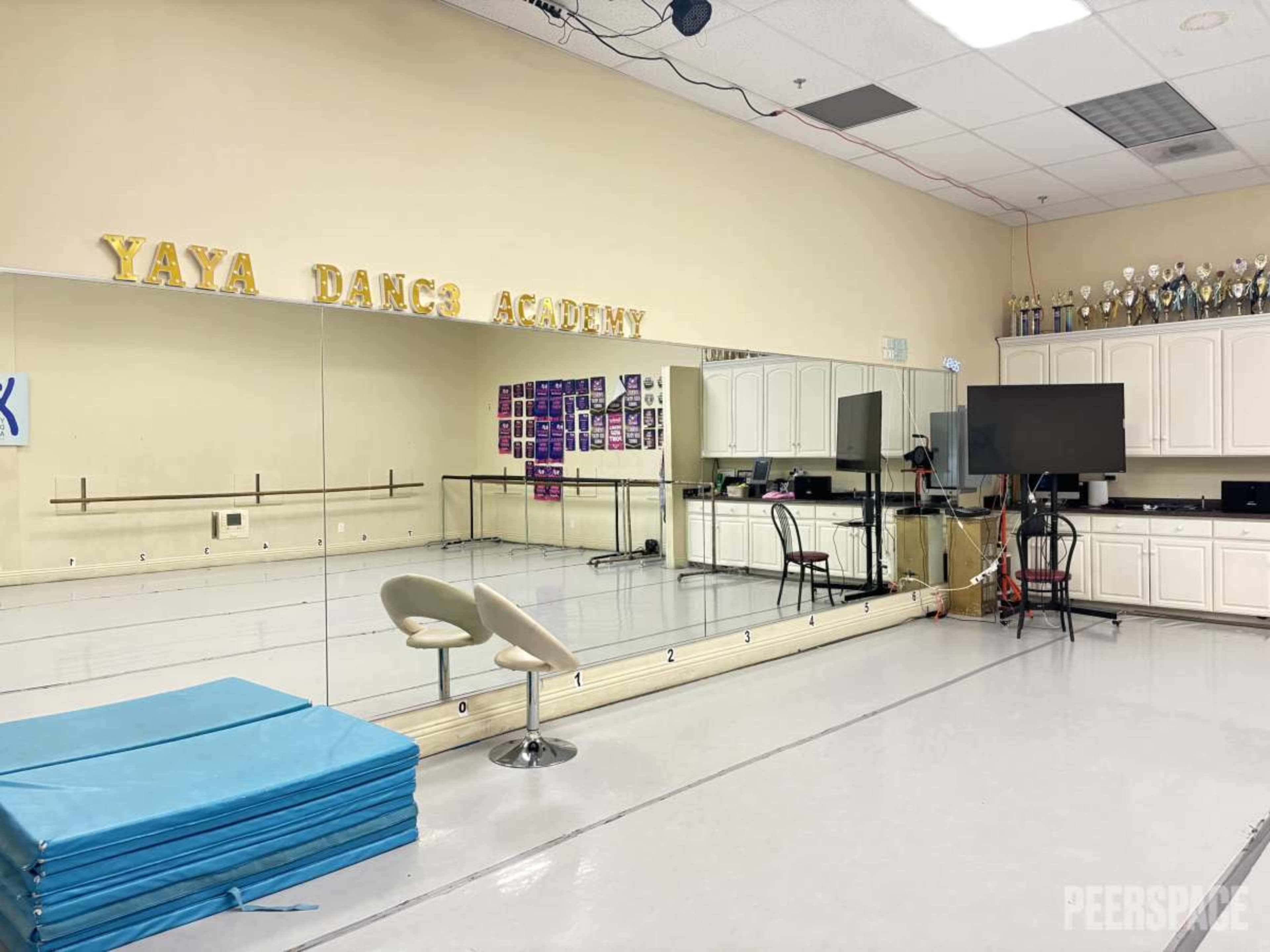 The image shows the interior of a dance studio with a mirrored wall, a ballet barre, and trophies displayed in cabinets.