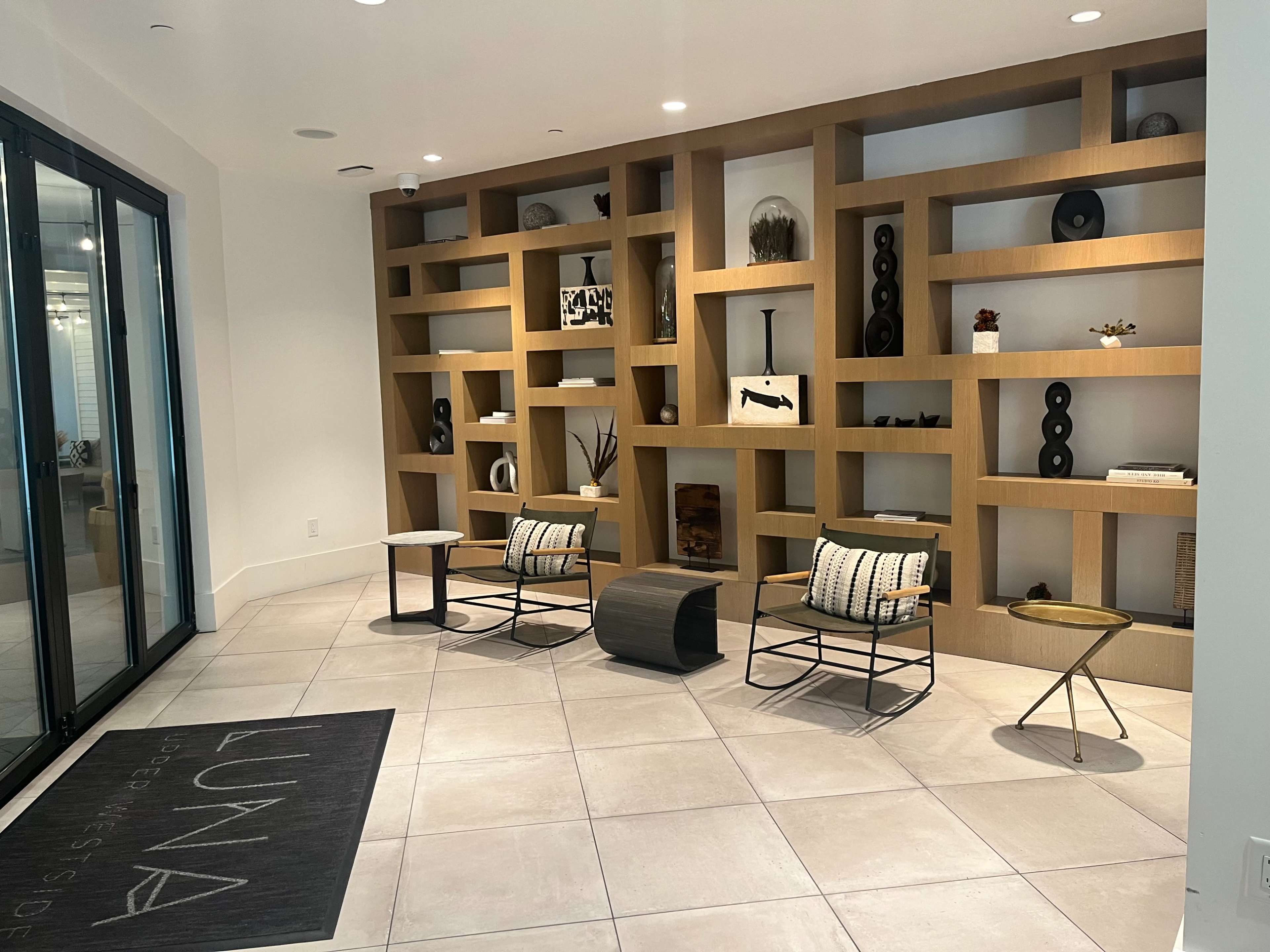 A modern lobby area featuring a decorative wooden shelving unit with various objects, two chairs, and a rug with the text "LUNA" on it.