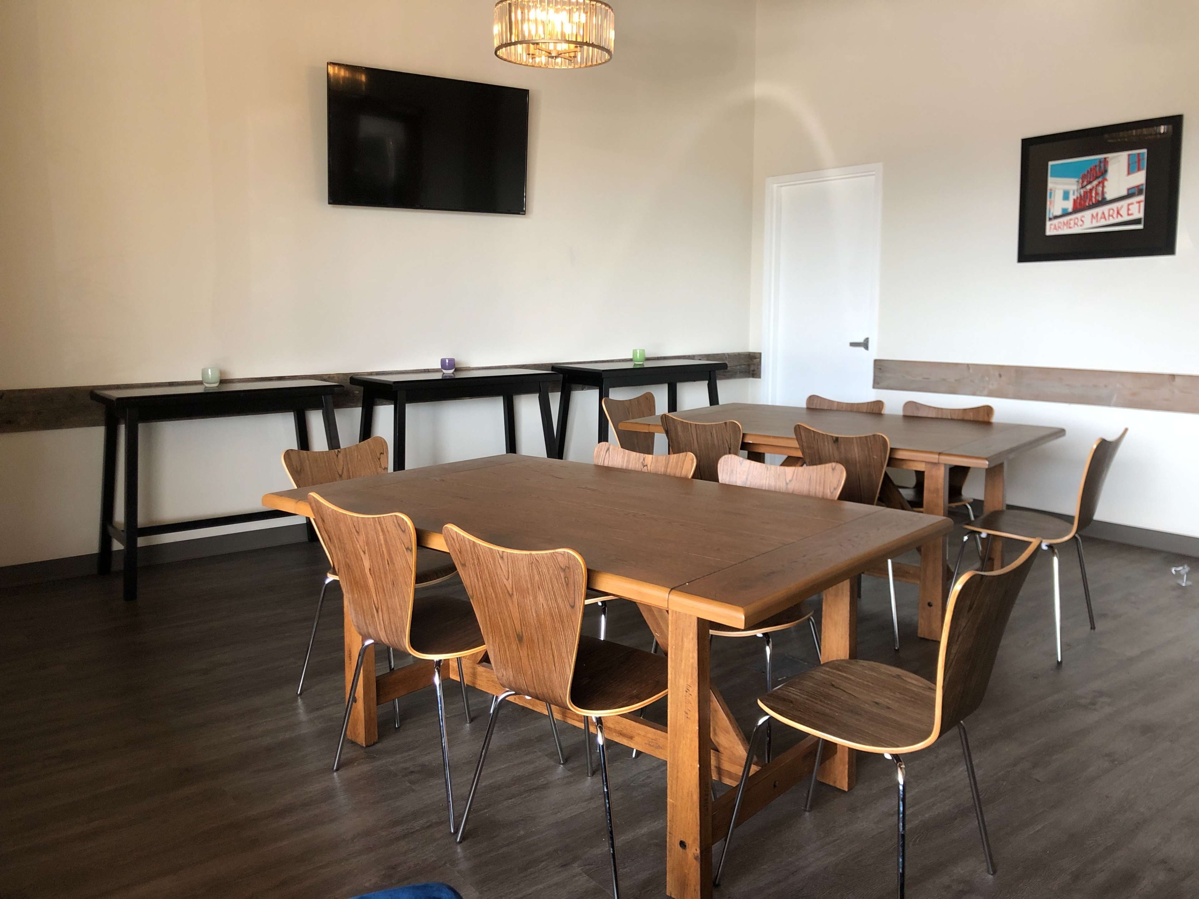 A minimalistic meeting room with several wooden tables and chairs arranged around the space, a wall-mounted TV, and decorative wall art.