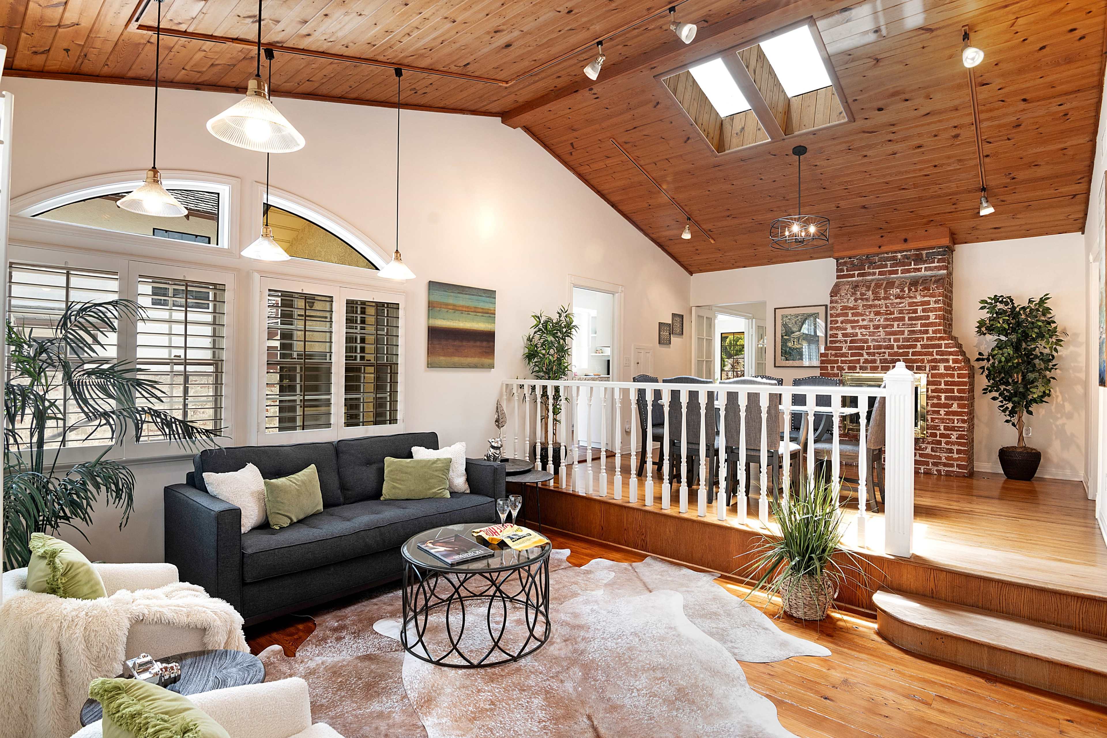 The image shows a cozy living room featuring a dark sofa, a round coffee table, and natural light coming through skylights and windows.