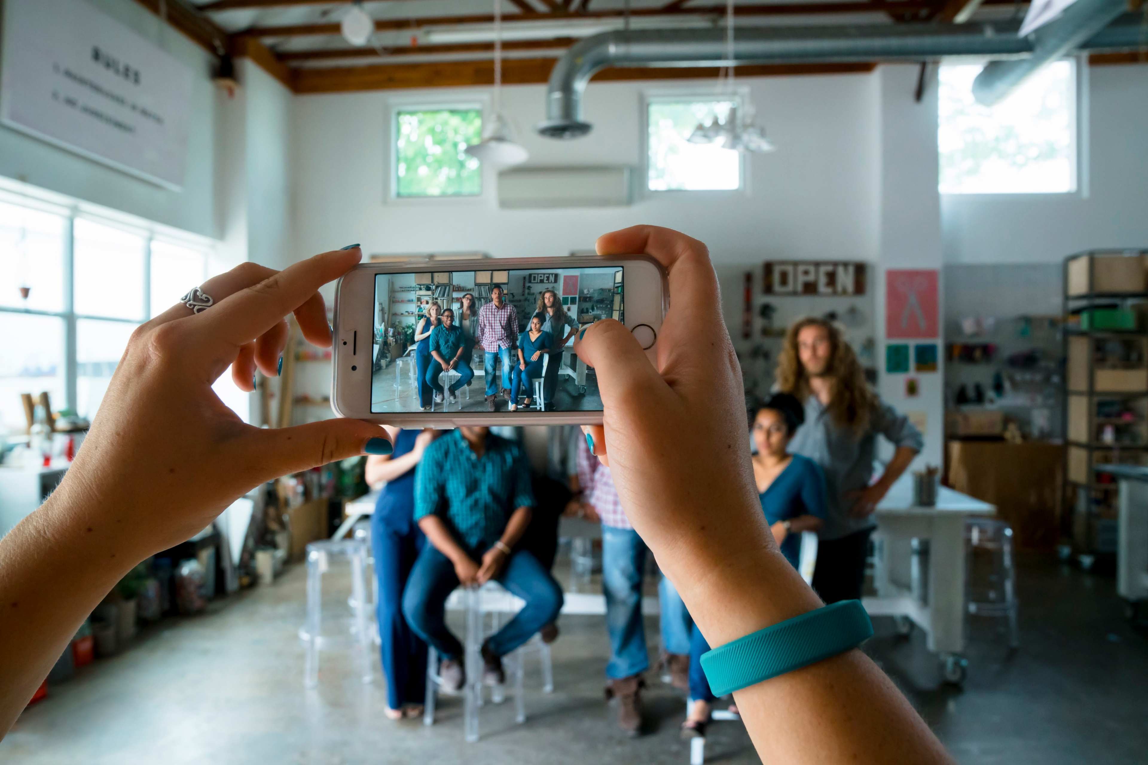 A person is taking a photo of a group of people sitting in a creative workspace.