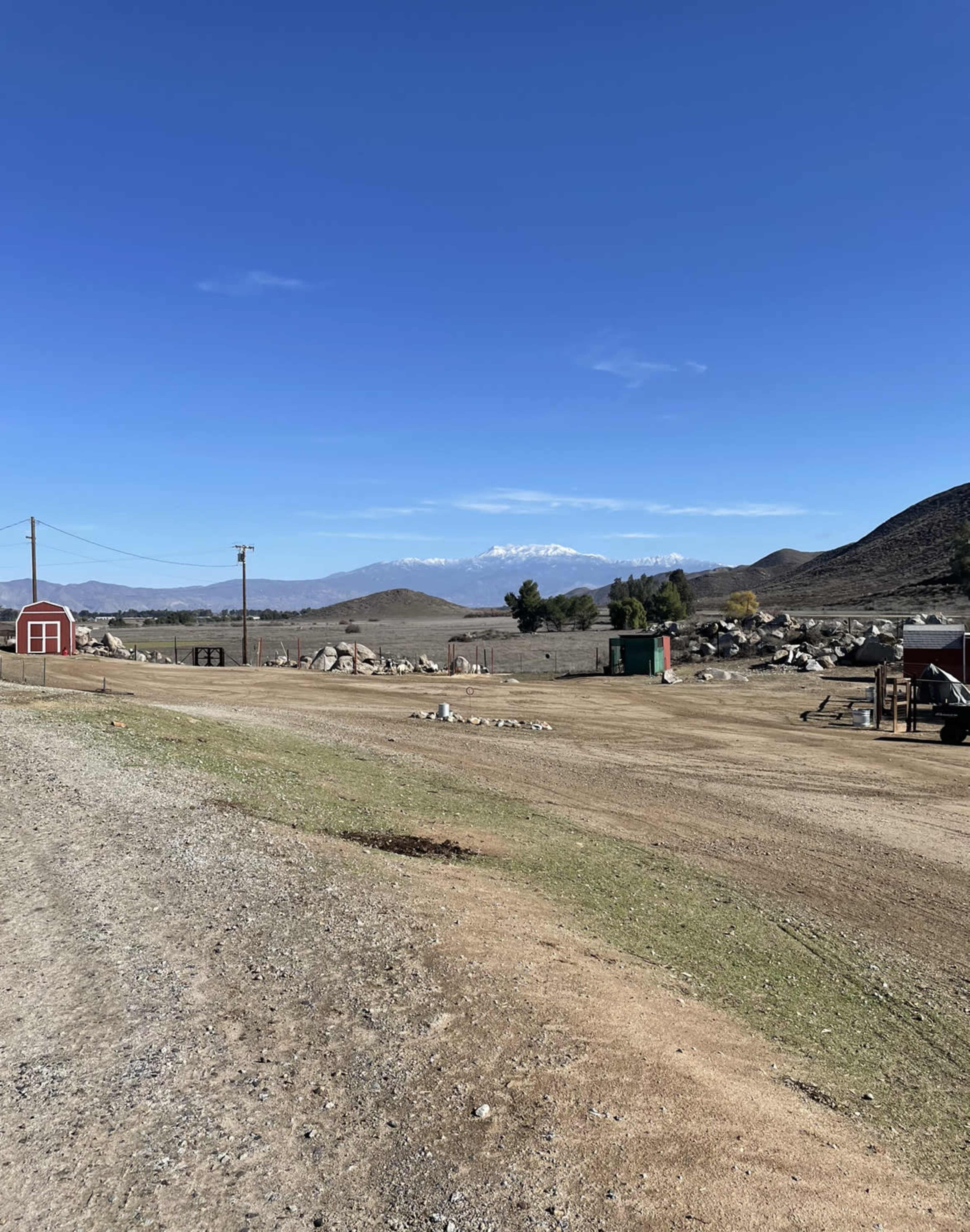 A gravel road leads through an open area with scattered rocks, a few structures, and distant mountains under a clear sky.