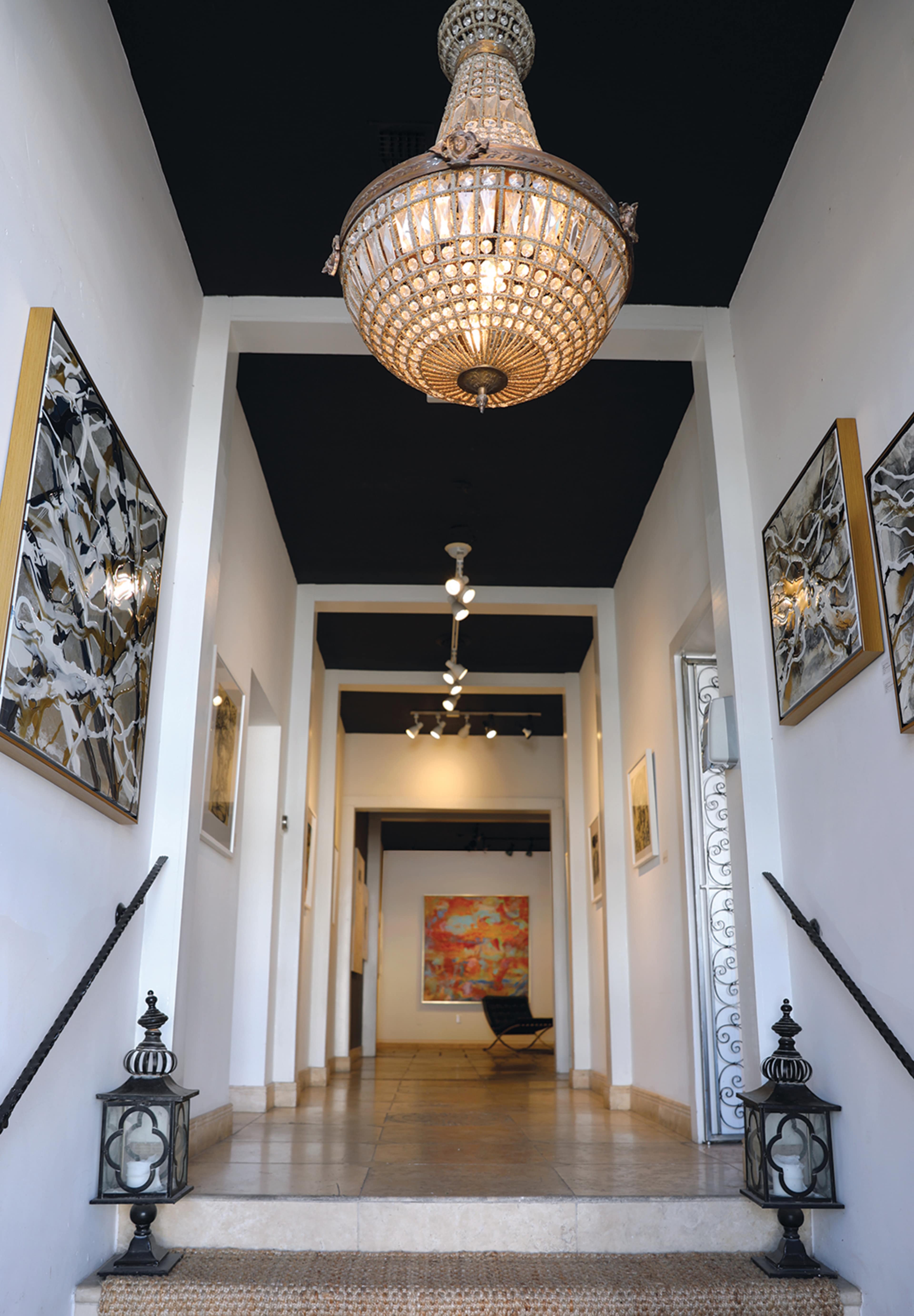 A wide hallway is illuminated by a chandelier, featuring framed artworks on the walls and decorative lanterns on the floor.