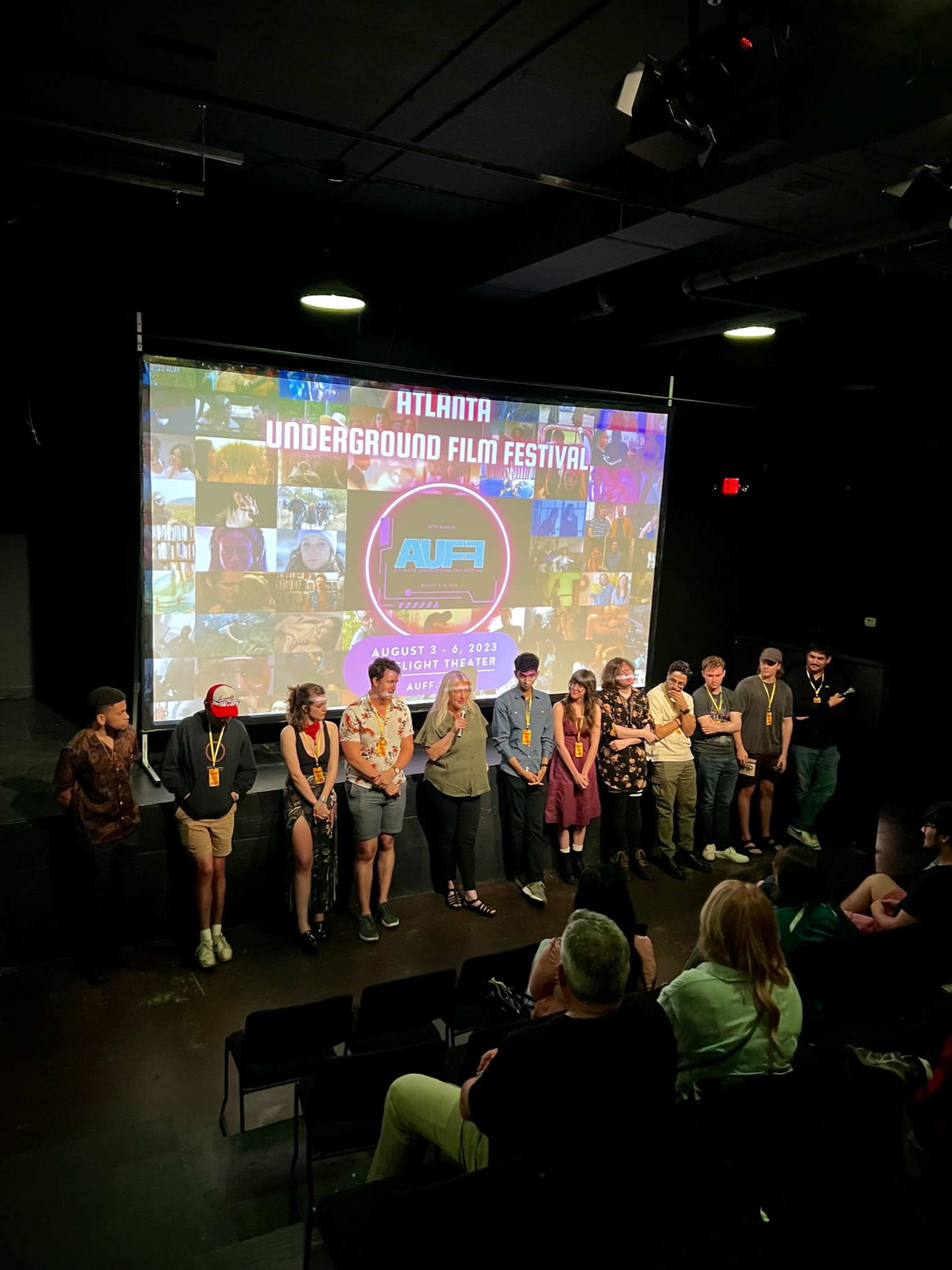 A group of individuals stands in front of a large screen displaying the logo and details of the Atlanta Underground Film Festival.