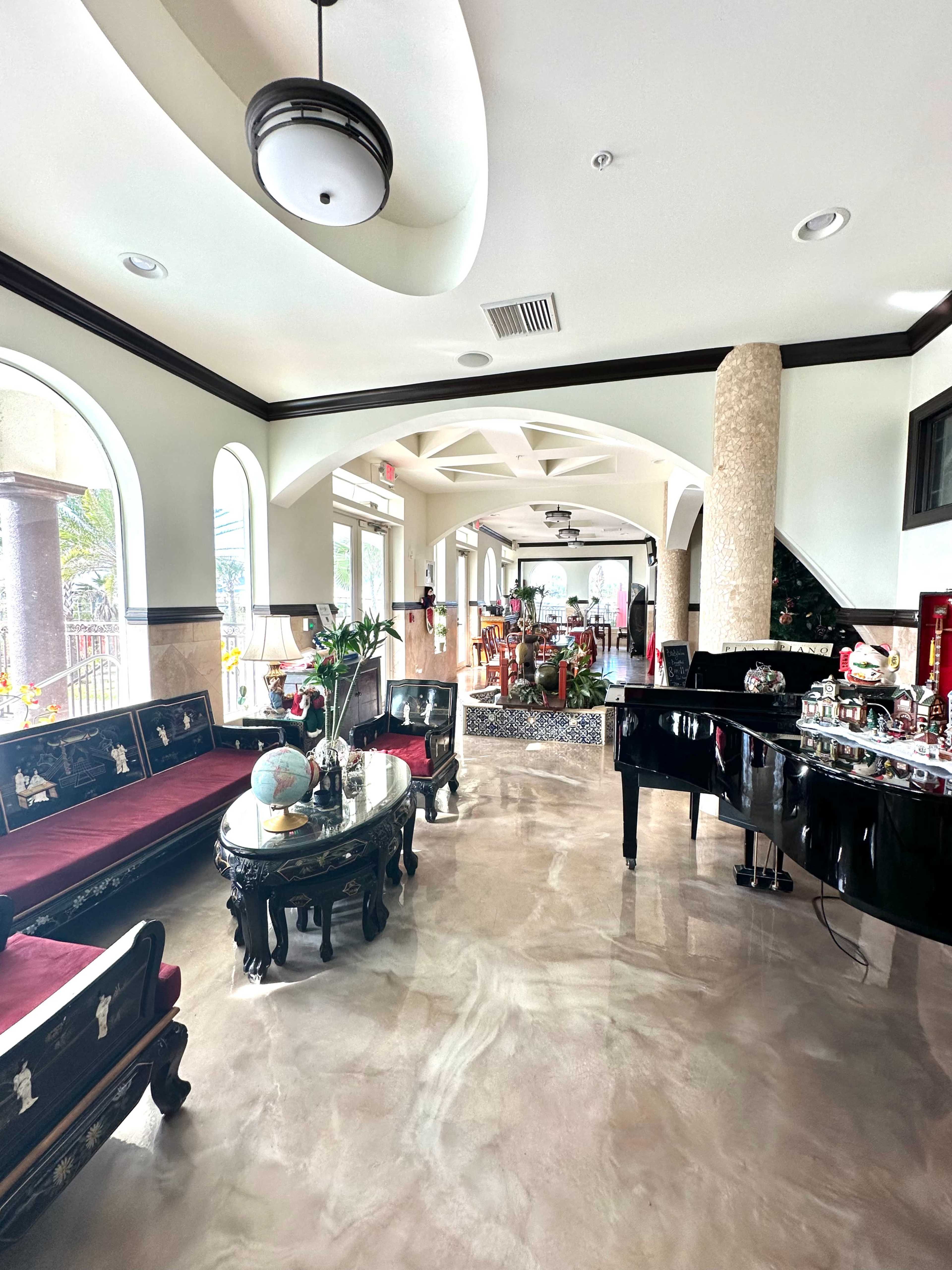 A spacious, elegantly decorated reception area featuring dark wooden furniture, a grand piano, and polished marble floors.