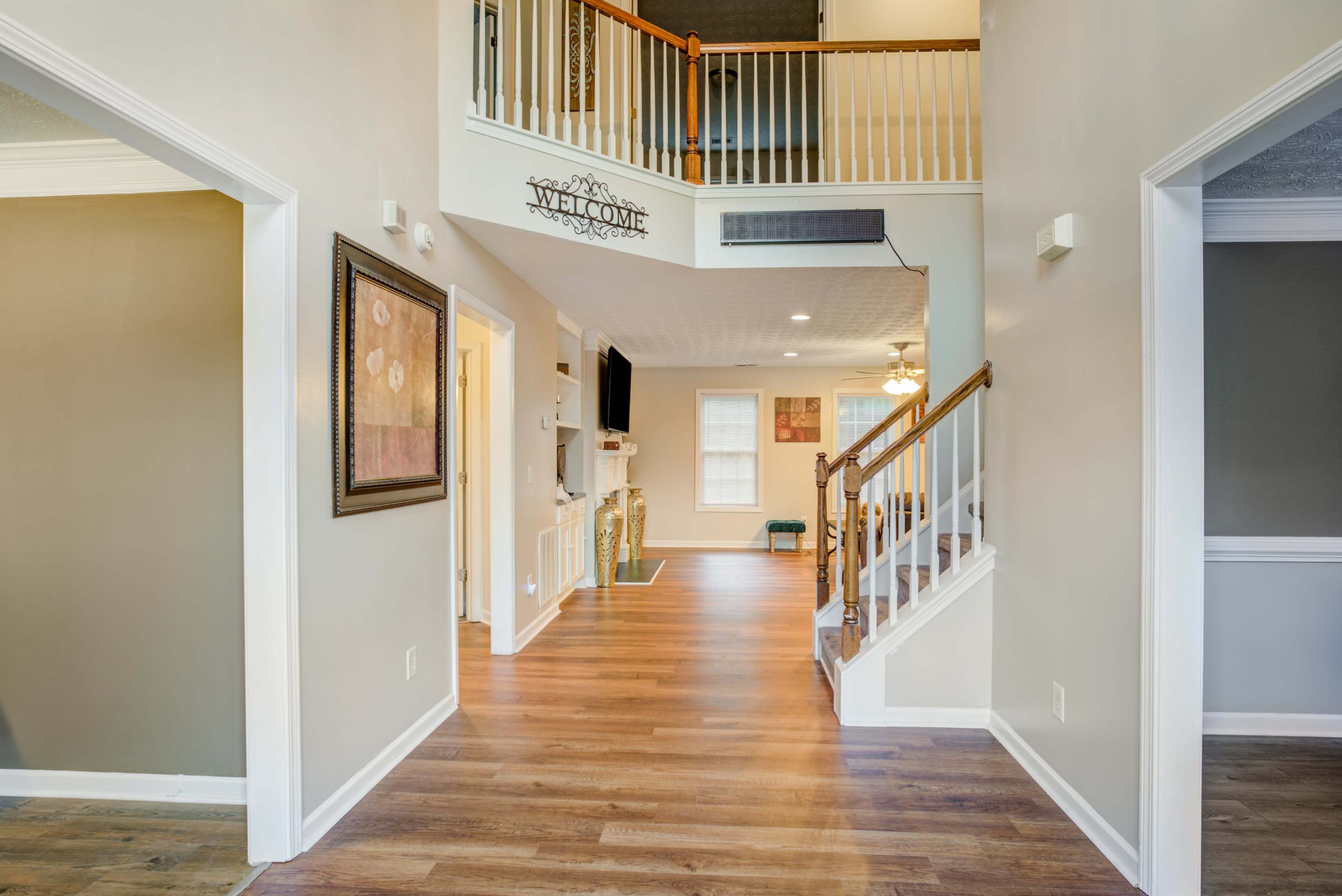 A bright, open foyer leading to a staircase, living area, and doorway to additional rooms in a house.