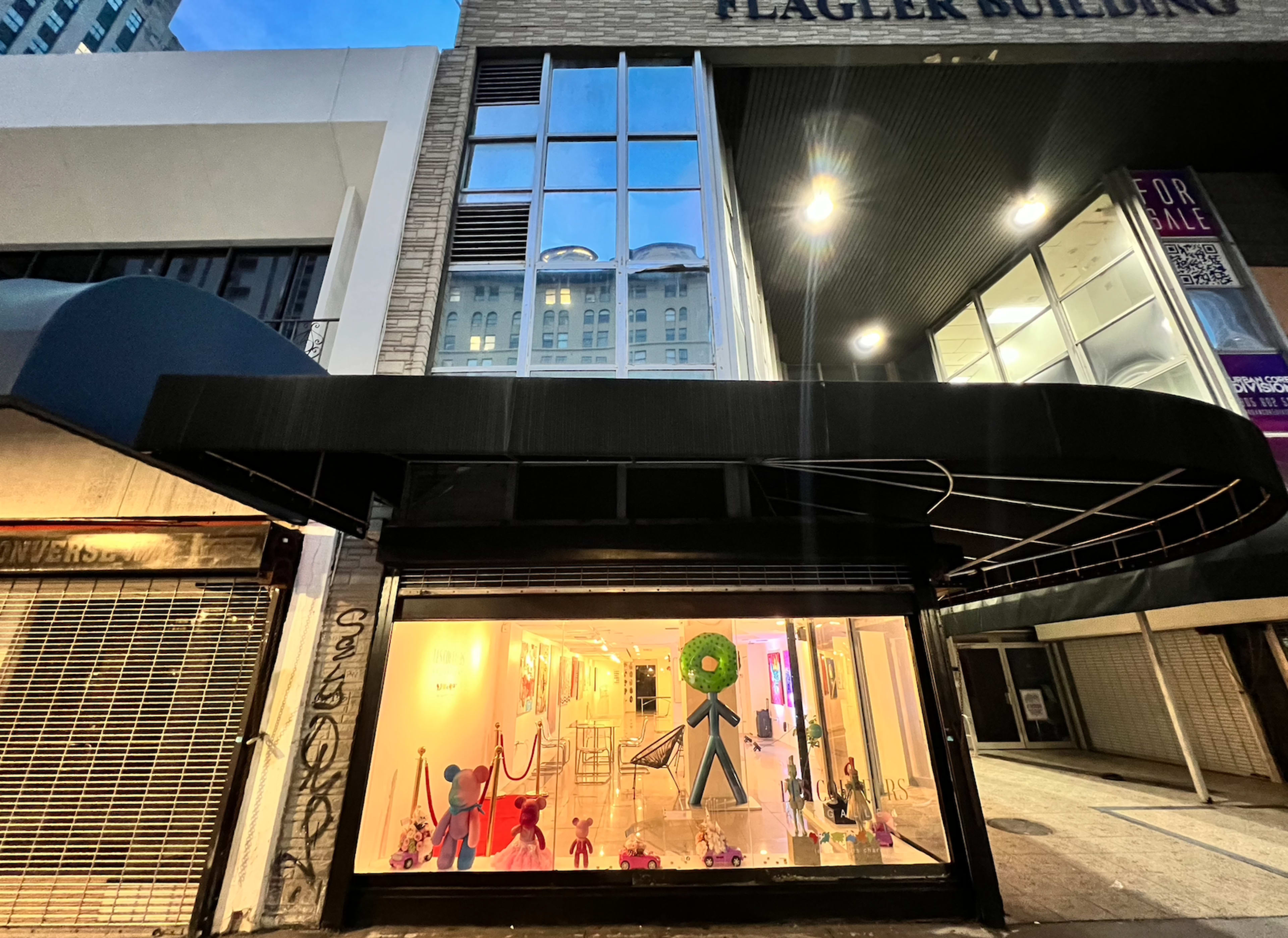 A storefront window showcases colorful decorations and a large green wreath, with the Flagler Building visible above.