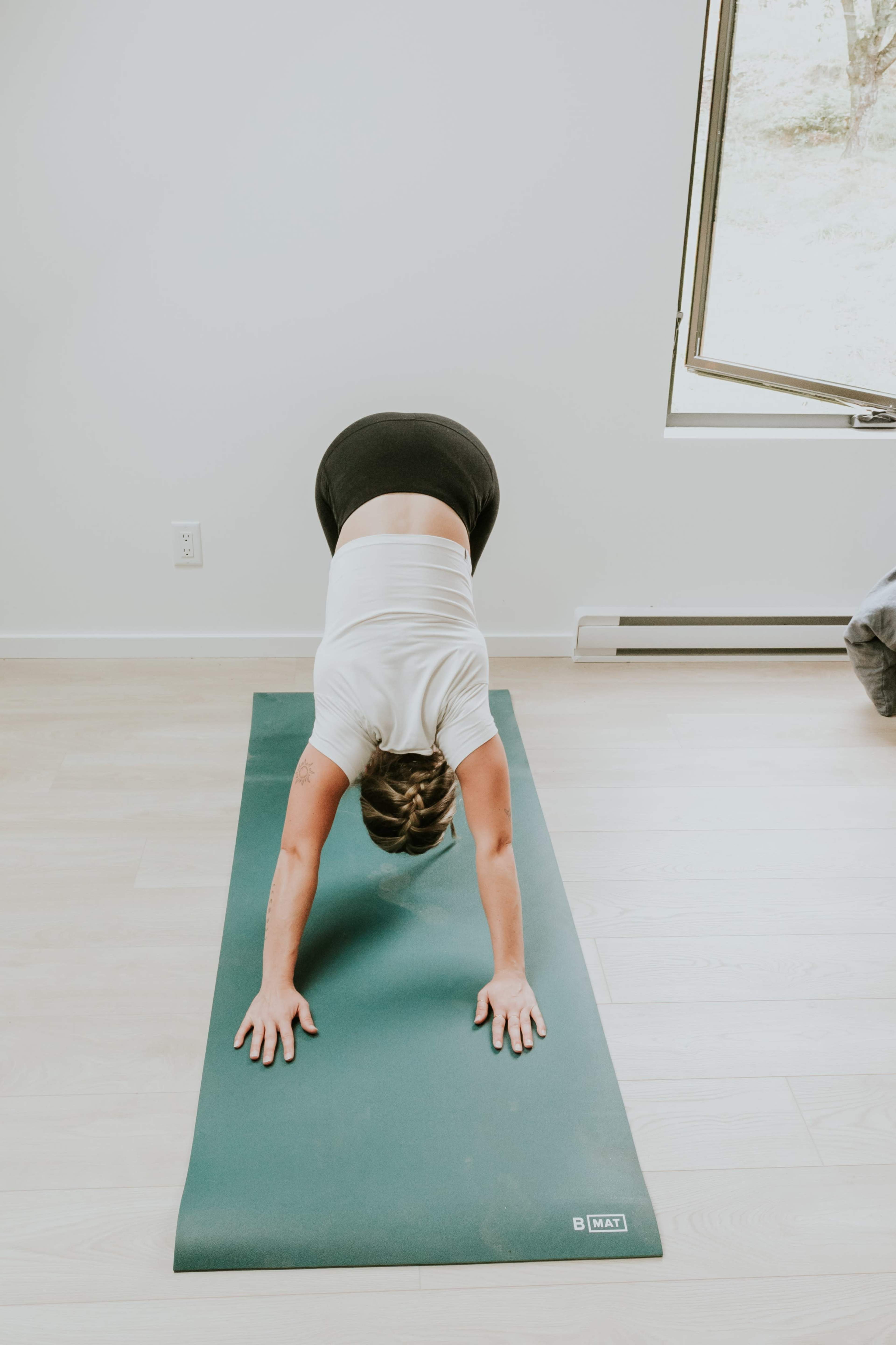A person is performing a downward dog pose on a green yoga mat in a well-lit room.