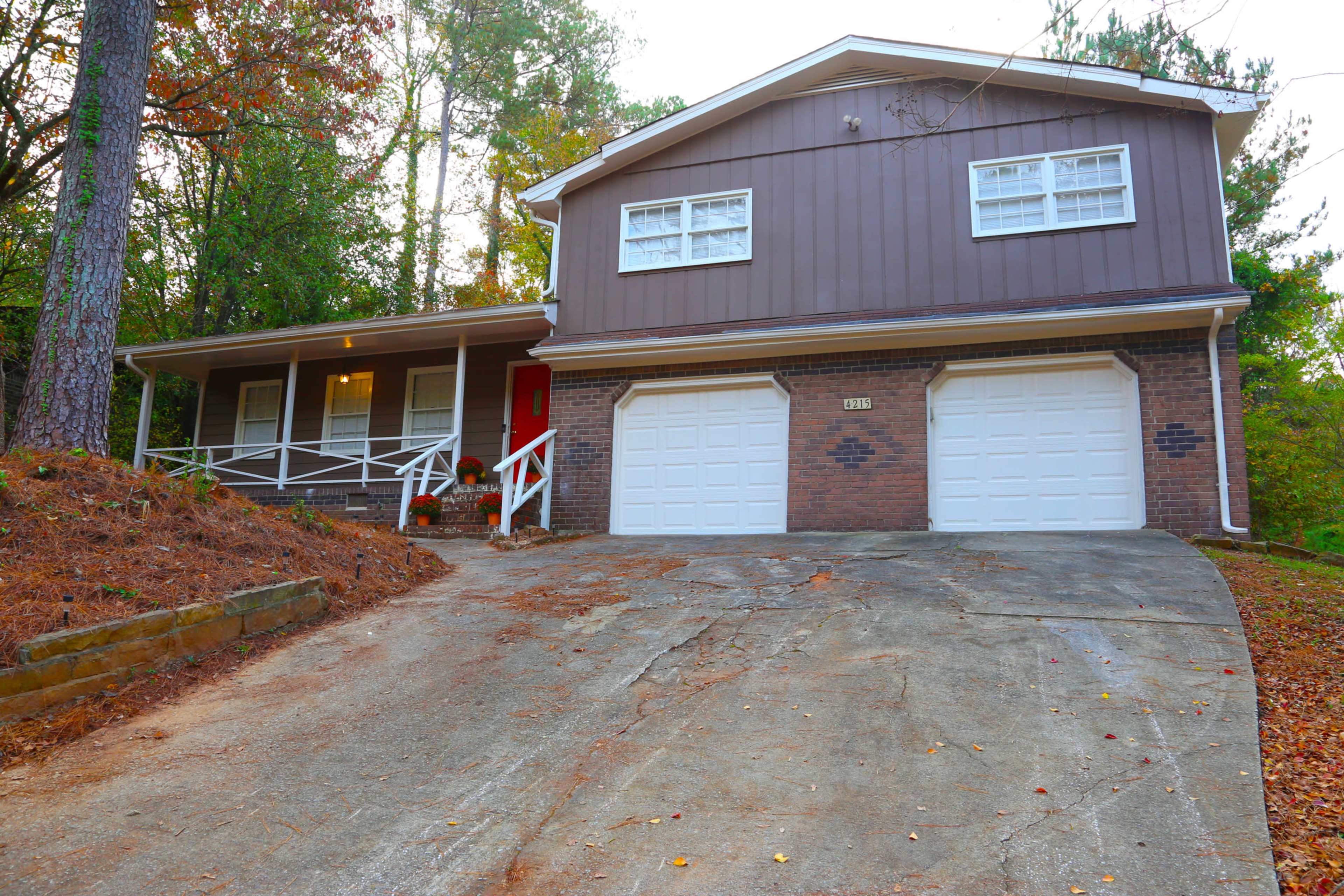 A two-story brown house with a front porch and a sloped driveway leading to a double garage.