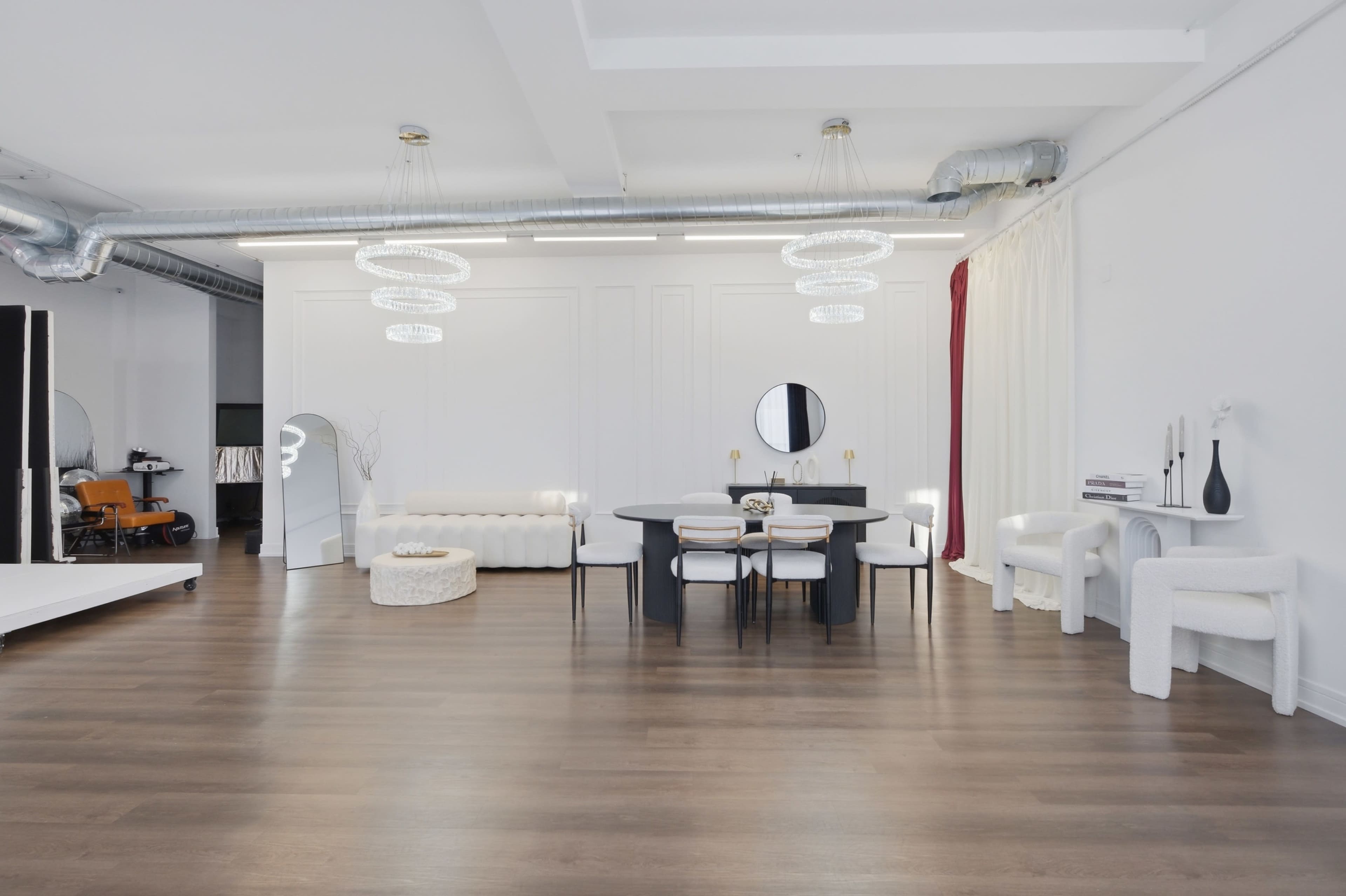 The image shows a spacious modern interior with a dining area featuring a round table surrounded by black chairs, complemented by a white sofa and minimalist decor.