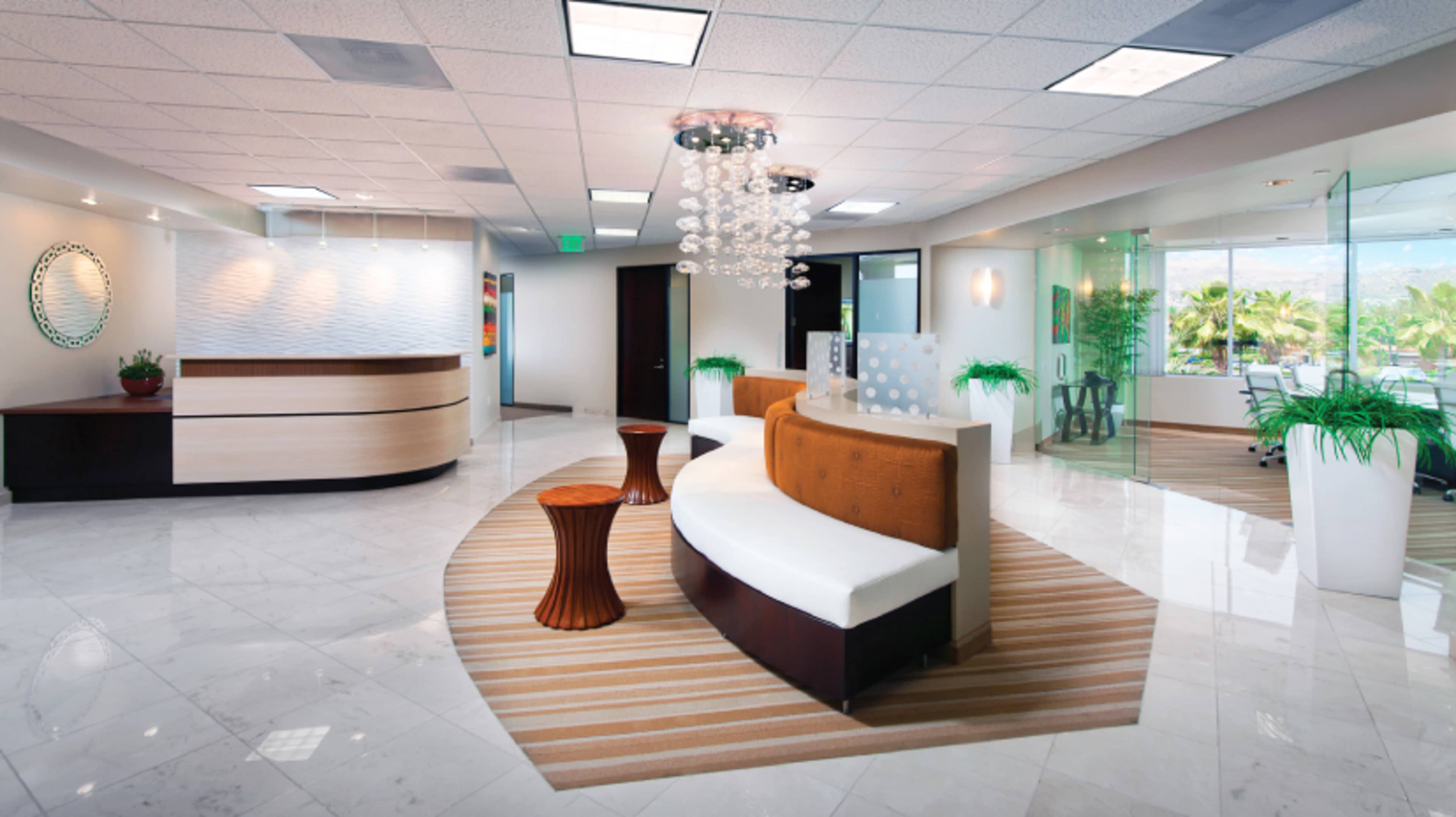 The image shows a modern reception area with white seating, a wooden accent table, and chrome light fixtures, set on glossy marble flooring.
