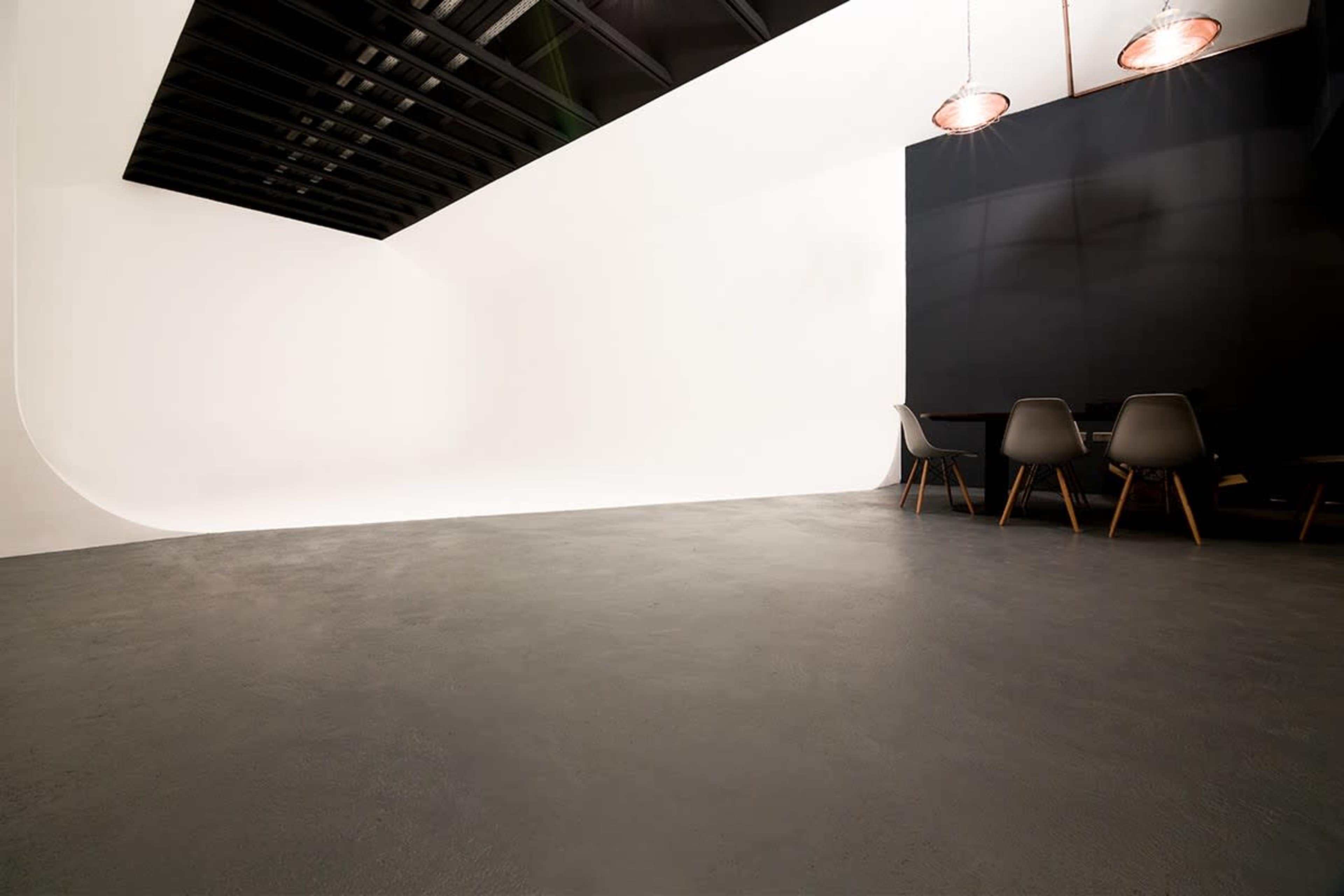 The image shows a modern studio space featuring a seamless white wall on one side and a black wall with a dining table and chairs on the other.