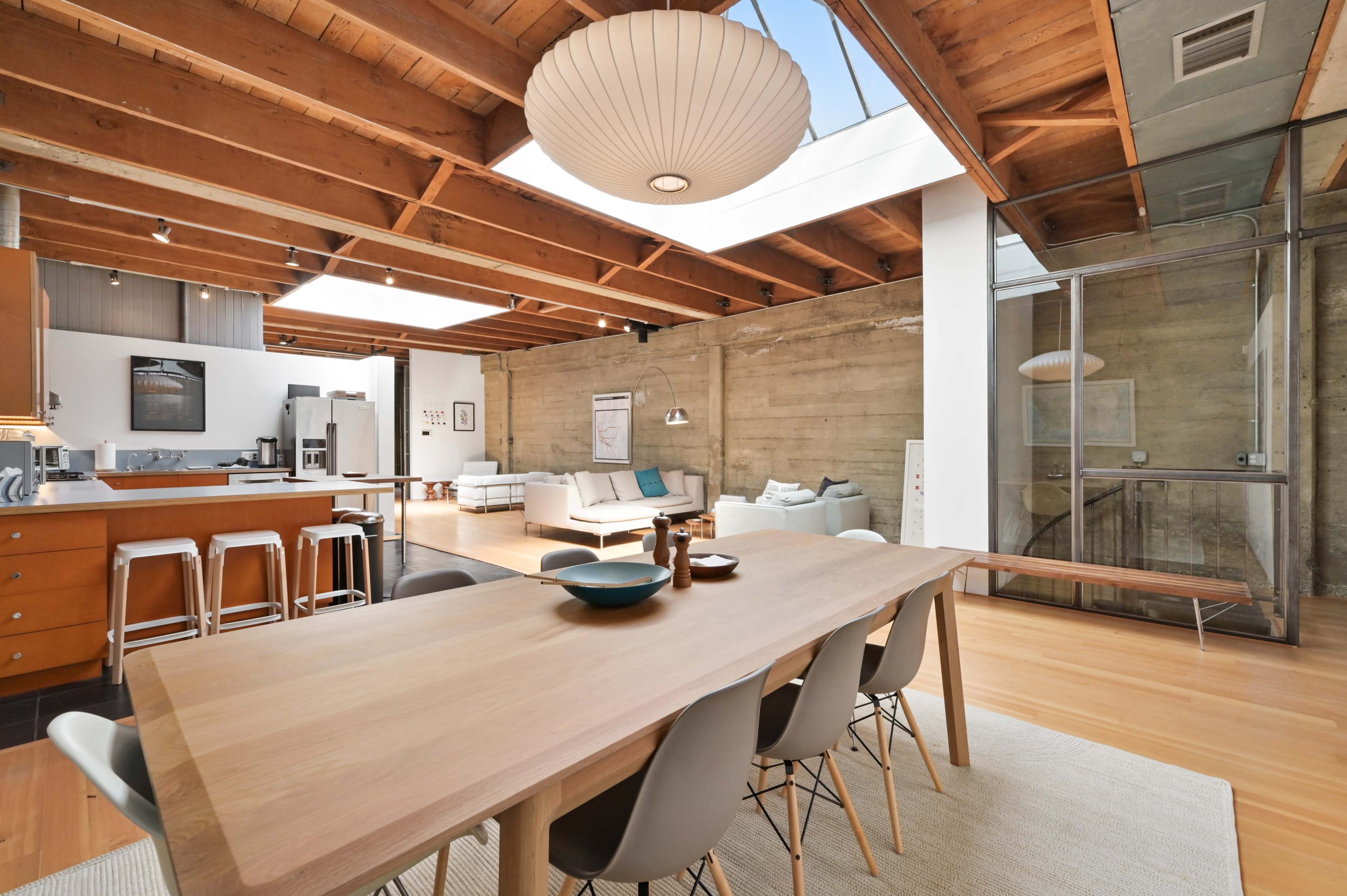 A spacious, modern open-concept living and dining area with wooden beams, a large dining table, and a bright seating area.