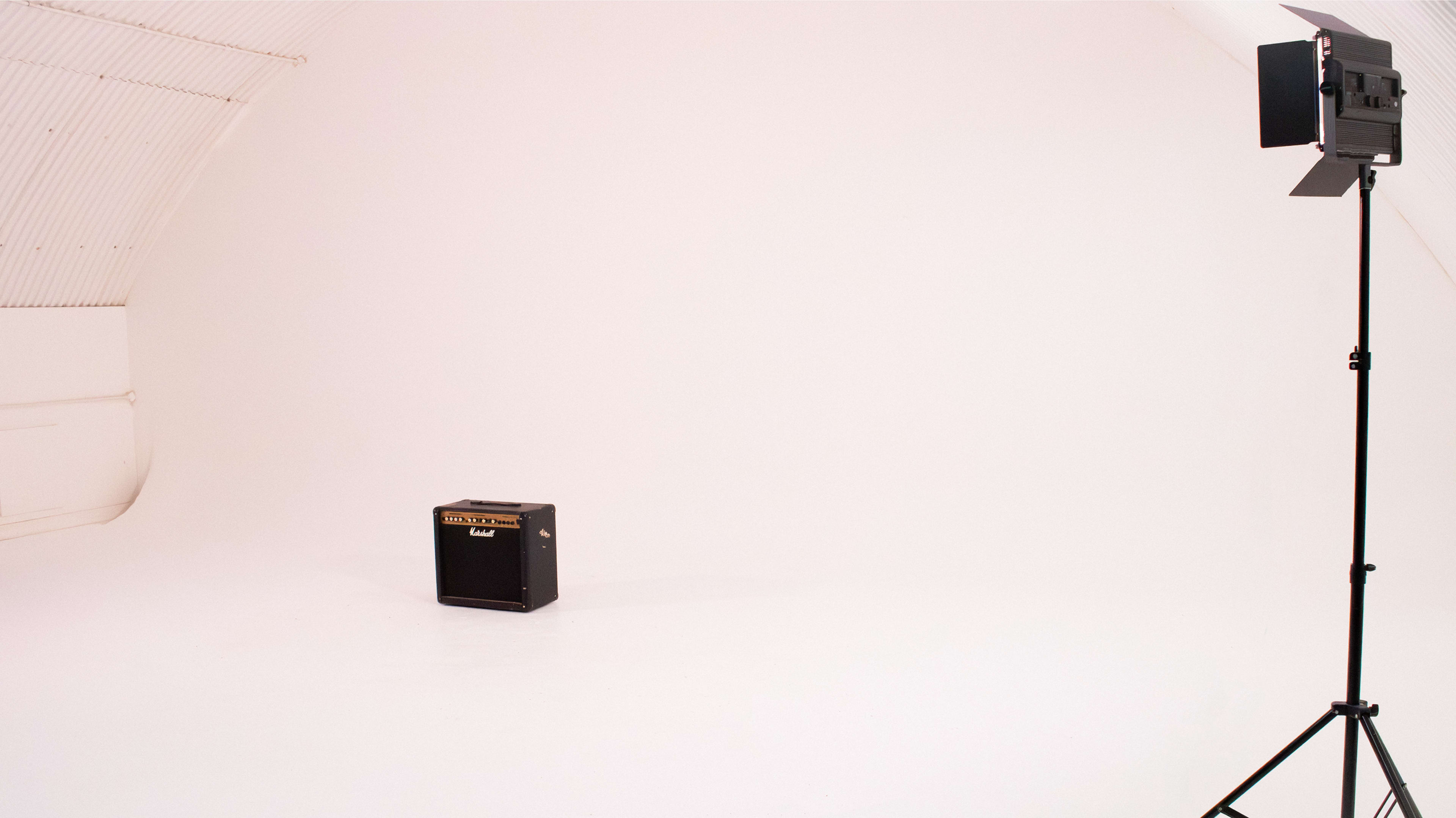 A black guitar amplifier positioned in a spacious, empty studio with white walls and a lighting setup on the right.