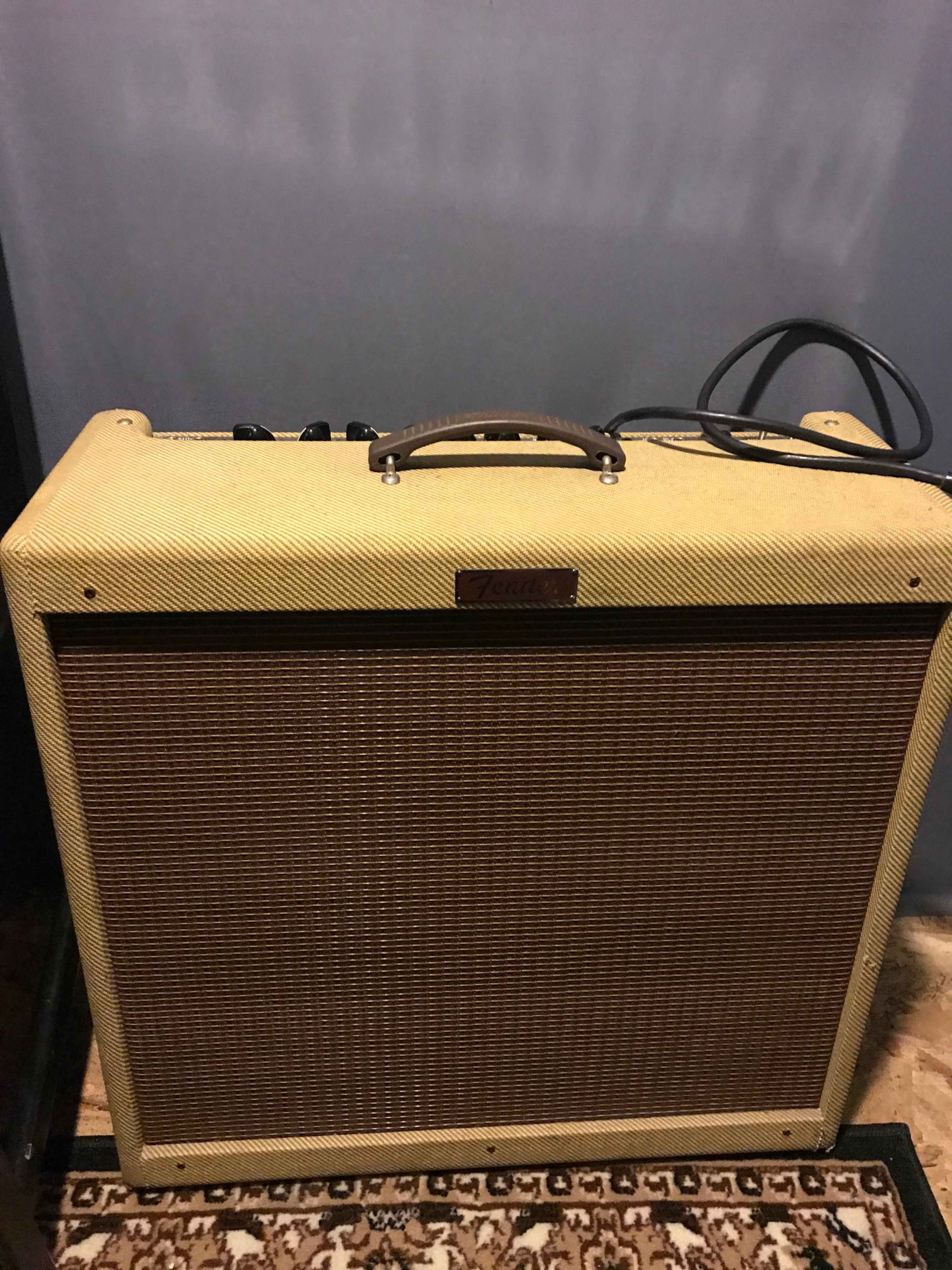 A vintage-style guitar amplifier with a textured tan and brown design is placed on a patterned rug against a grey wall.