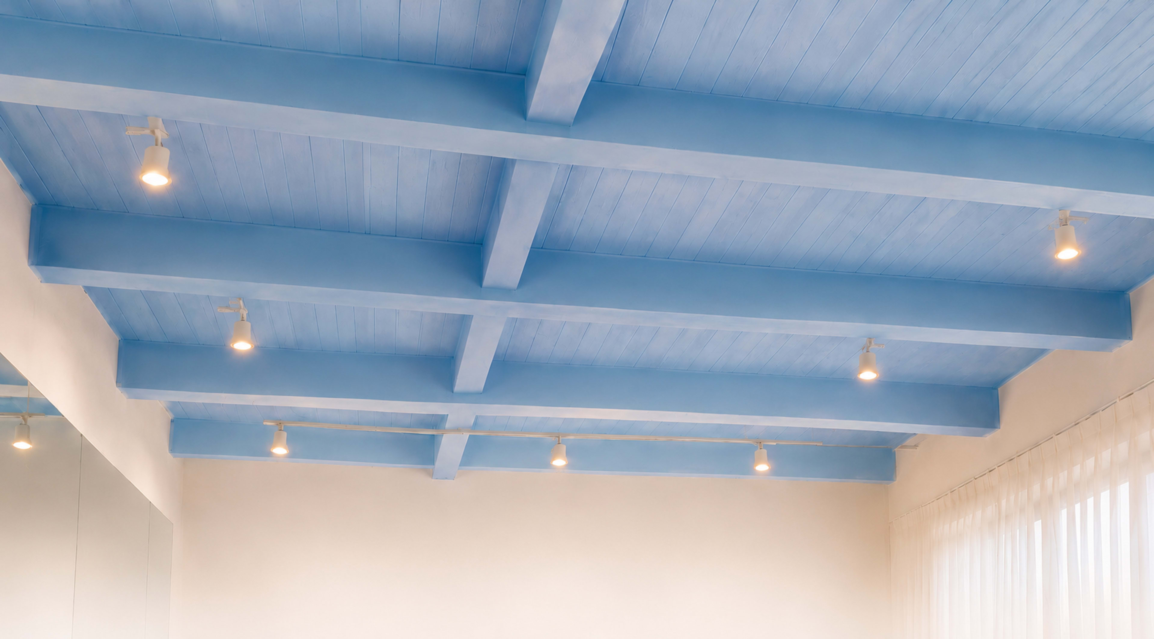 The image shows a room with a blue-beamed ceiling and evenly spaced spotlights illuminating the space, along with a large mirror reflecting a portion of the room.