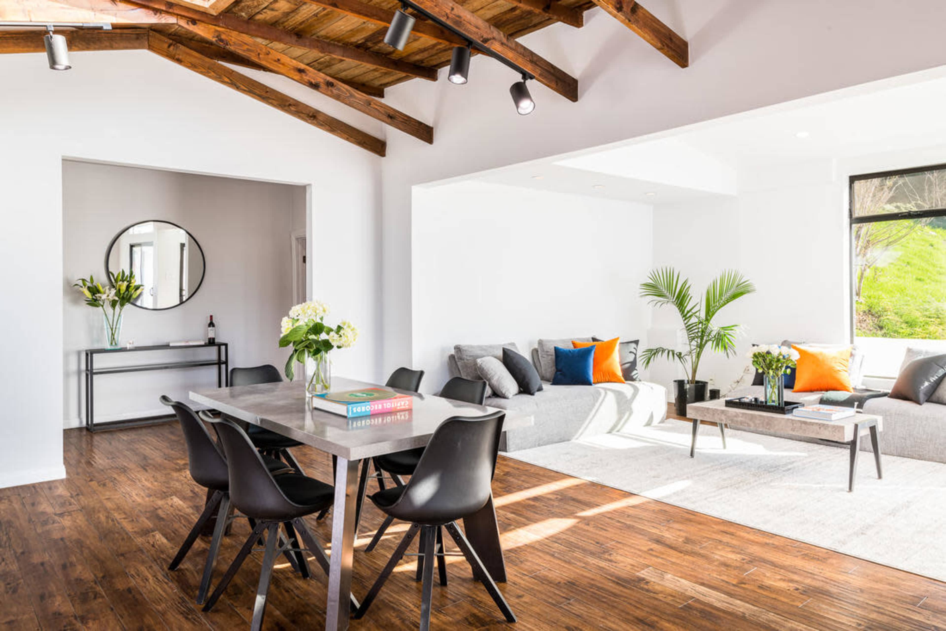 A modern open-concept living area with a dining table, chairs, and a seating area featuring a gray sofa and decorative pillows.