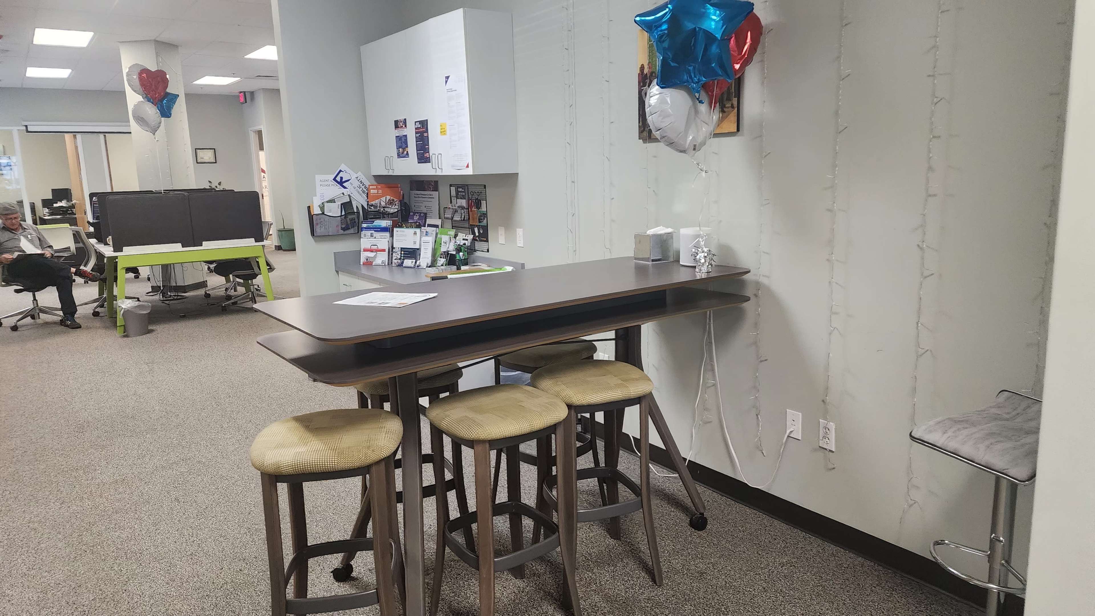 A small kitchenette area with a high table and stools, decorated with balloons, in an office environment.