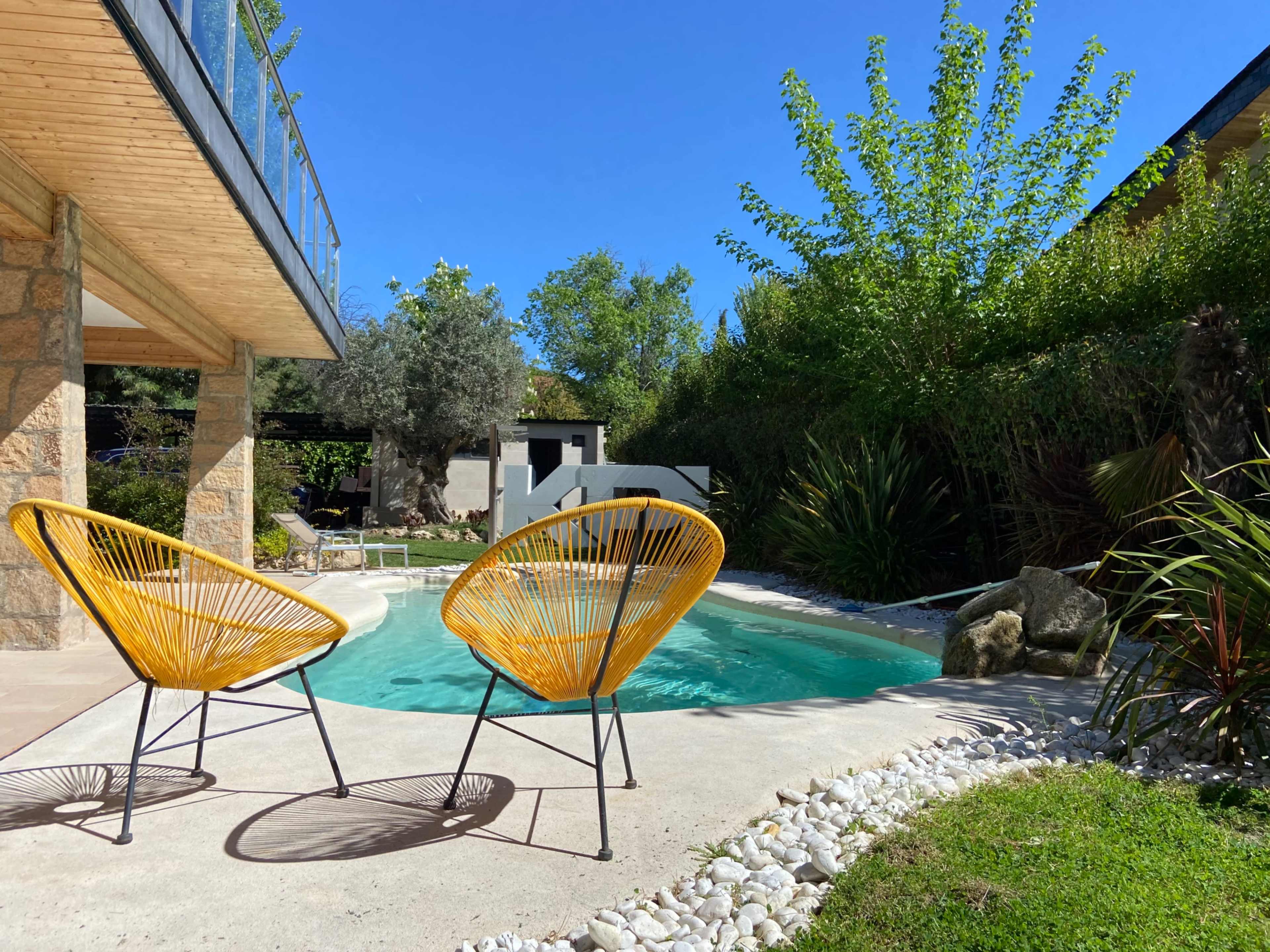 A pair of yellow chairs overlooks a small, curved swimming pool surrounded by greenery and a stone structure in the background.
