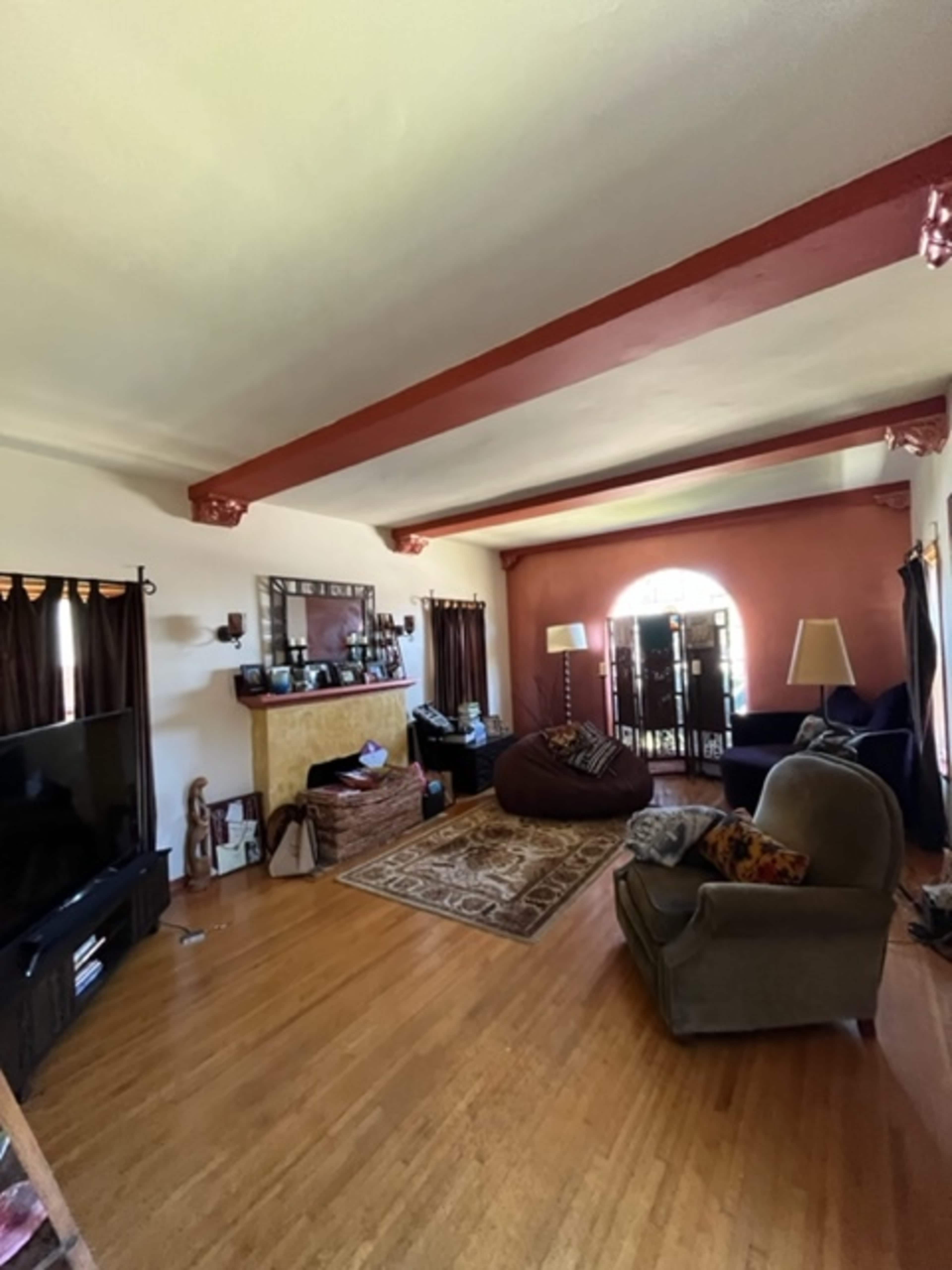The image shows a living room with wooden flooring, a television, a large bean bag, and a mix of furniture including a chair and a sofa, along with a fireplace and decorative items on shelves.