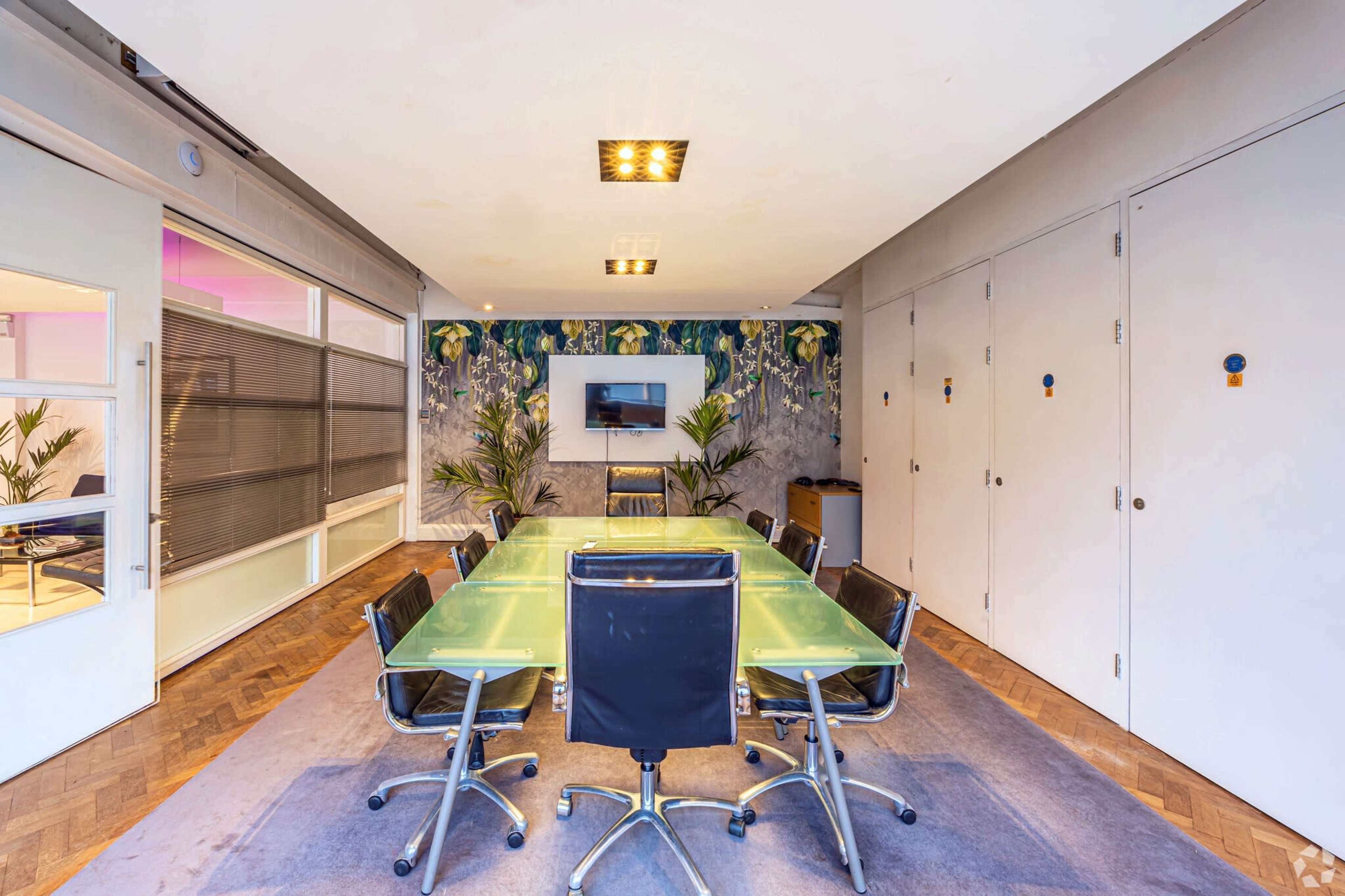 A modern conference room features a glass table surrounded by black chairs, with a large wall-mounted screen and decorative wall art.