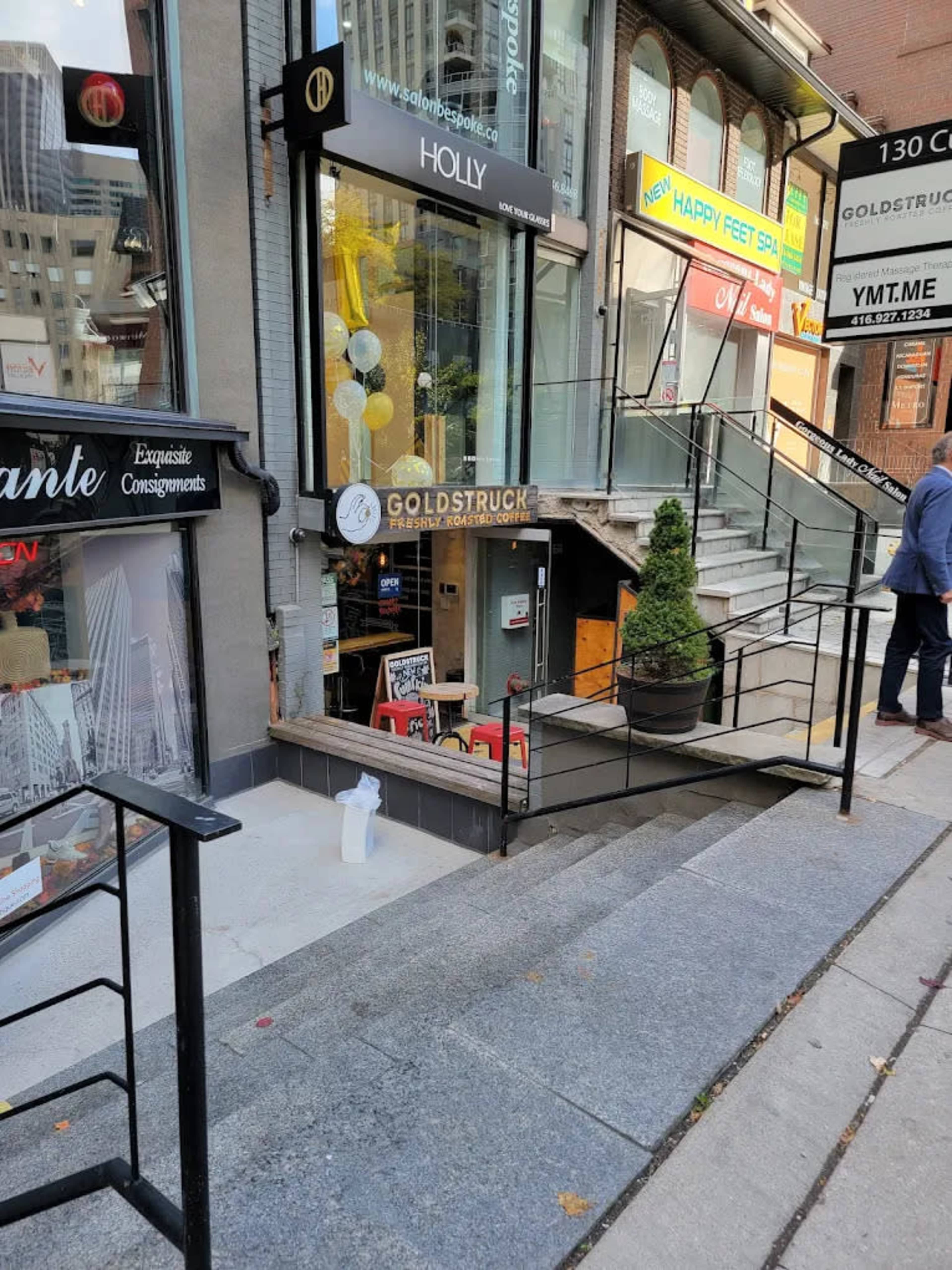 The image shows a storefront with the sign "GOLDSTRUCK" and a staircase leading down to the entrance, alongside various signage for nearby businesses.