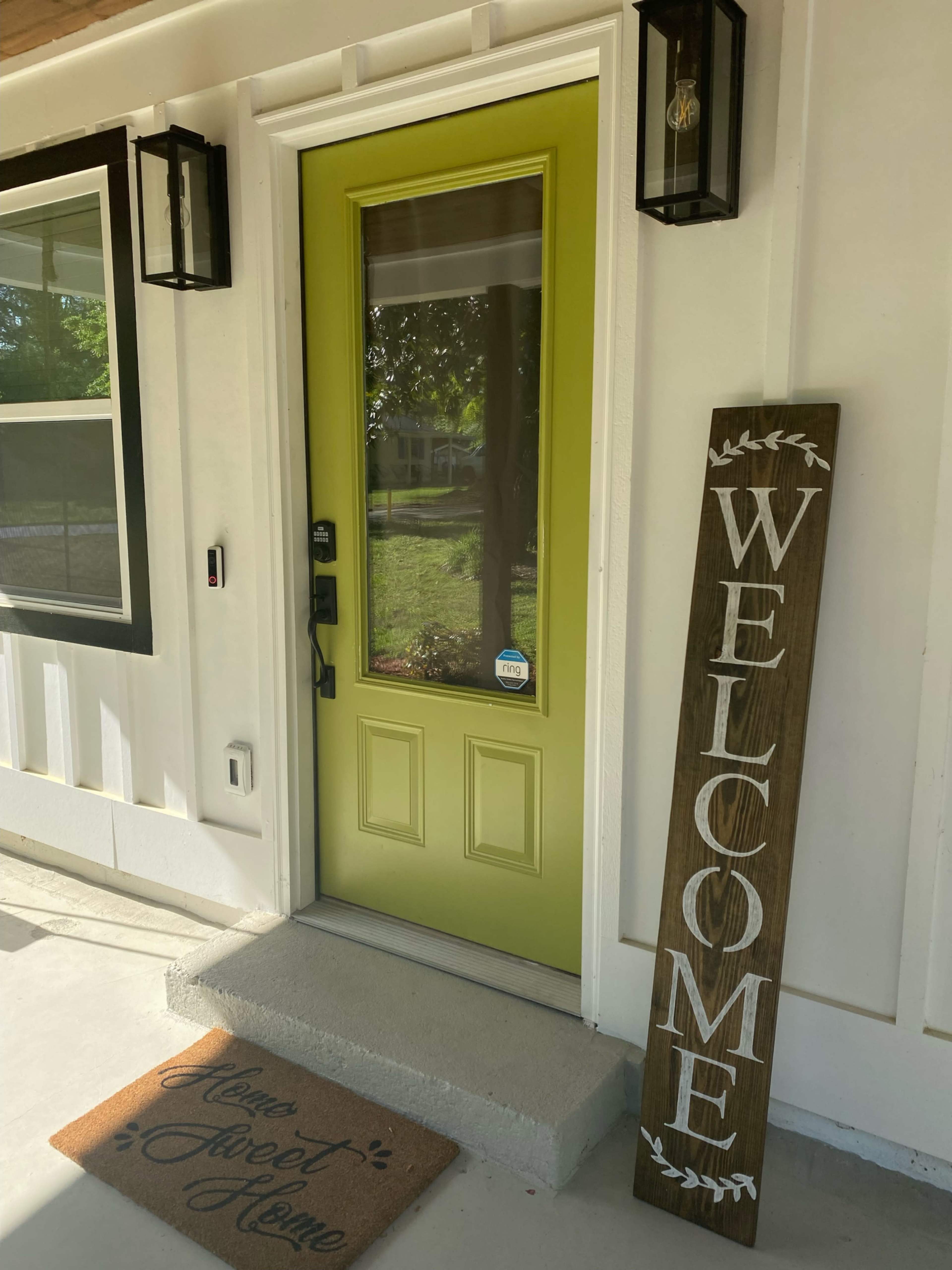 The image shows a bright green front door with a welcome sign and a "Home Sweet Home" doormat at the entrance of a house.