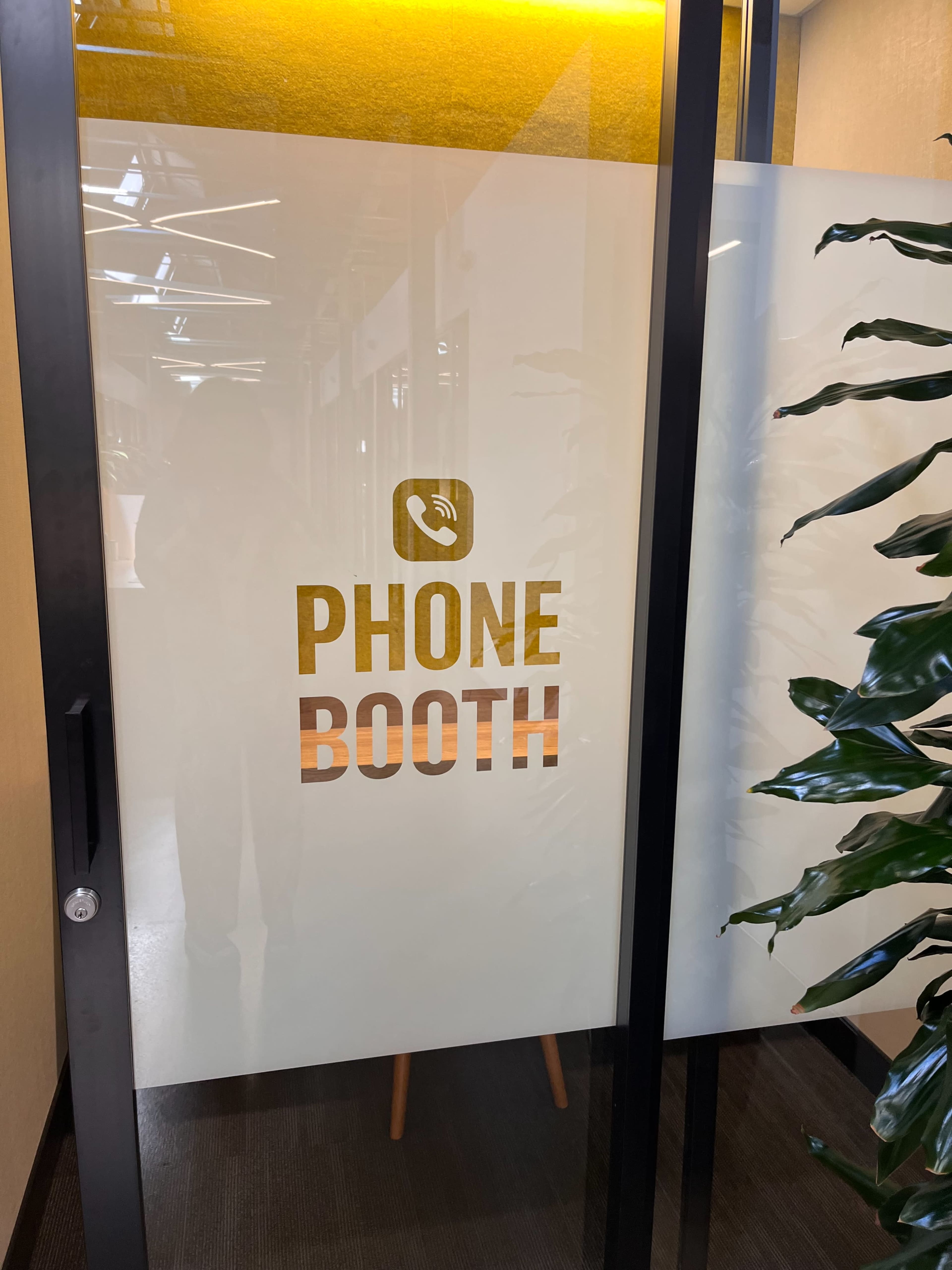 A glass door with a frosted design, featuring the words "PHONE BOOTH" in bold, golden letters.