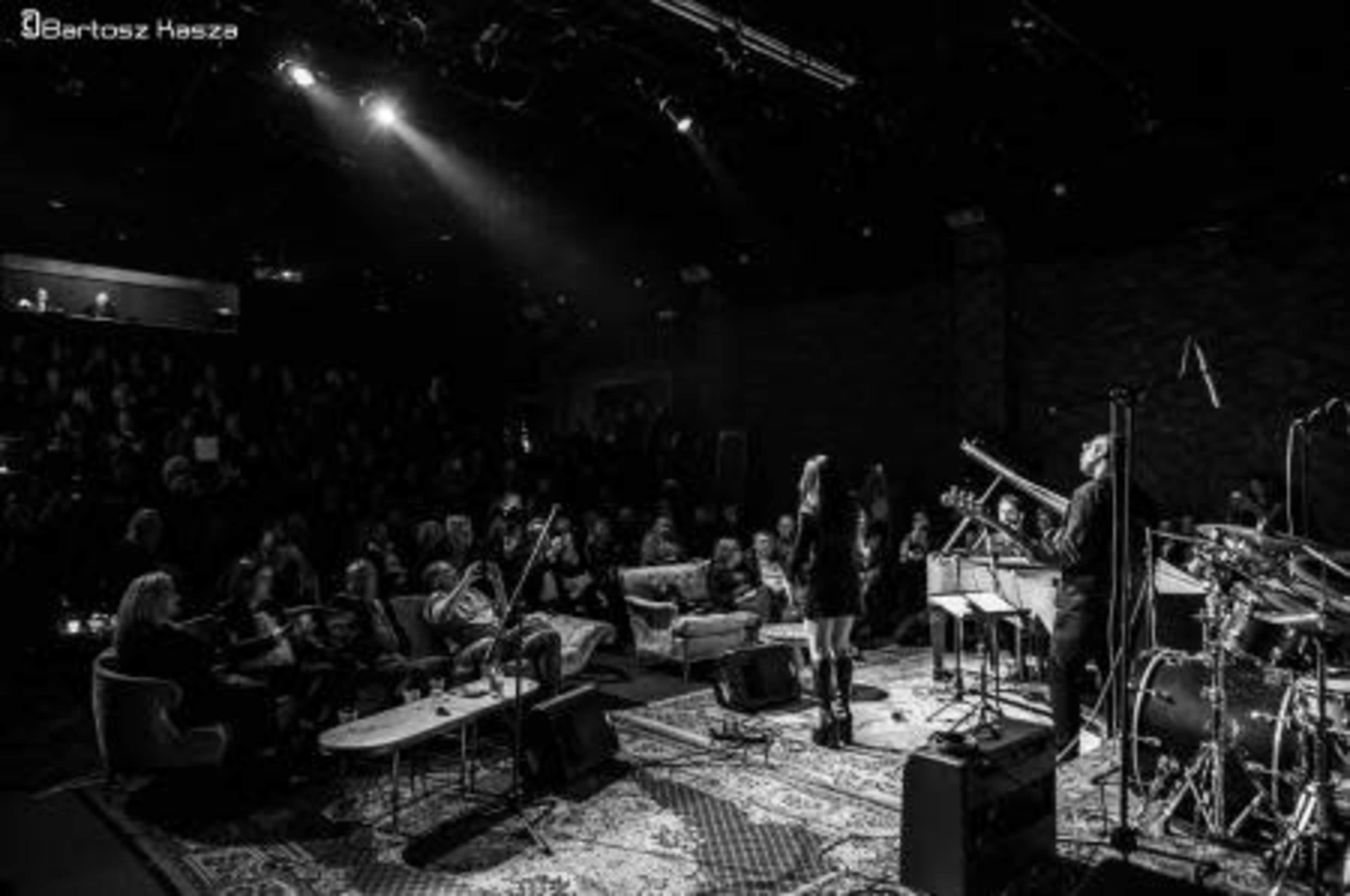 A diverse audience watches a live music performance on stage in a dimly lit venue.