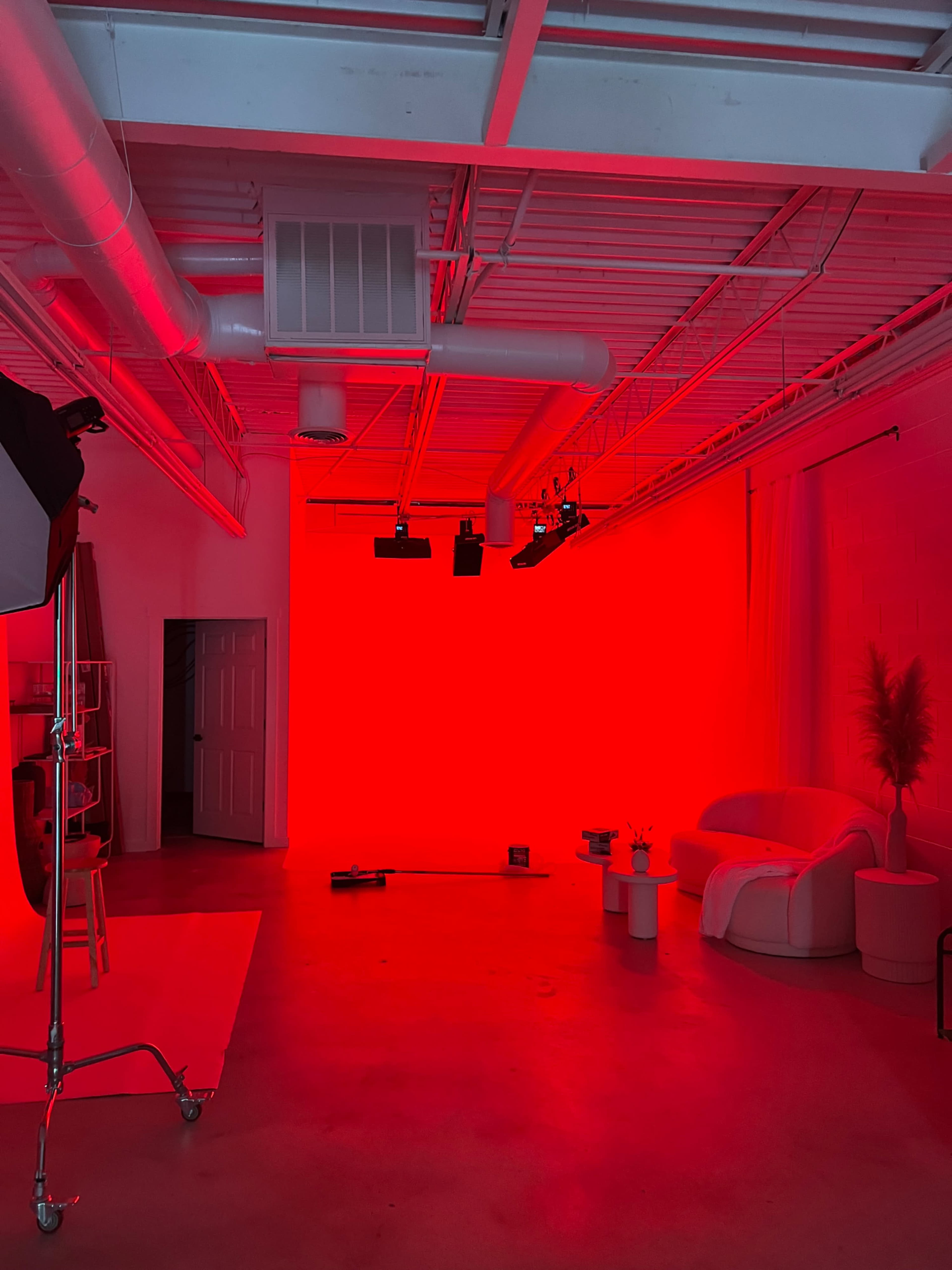 A studio space with a red backdrop, a white couch, a plant, and various lighting equipment.
