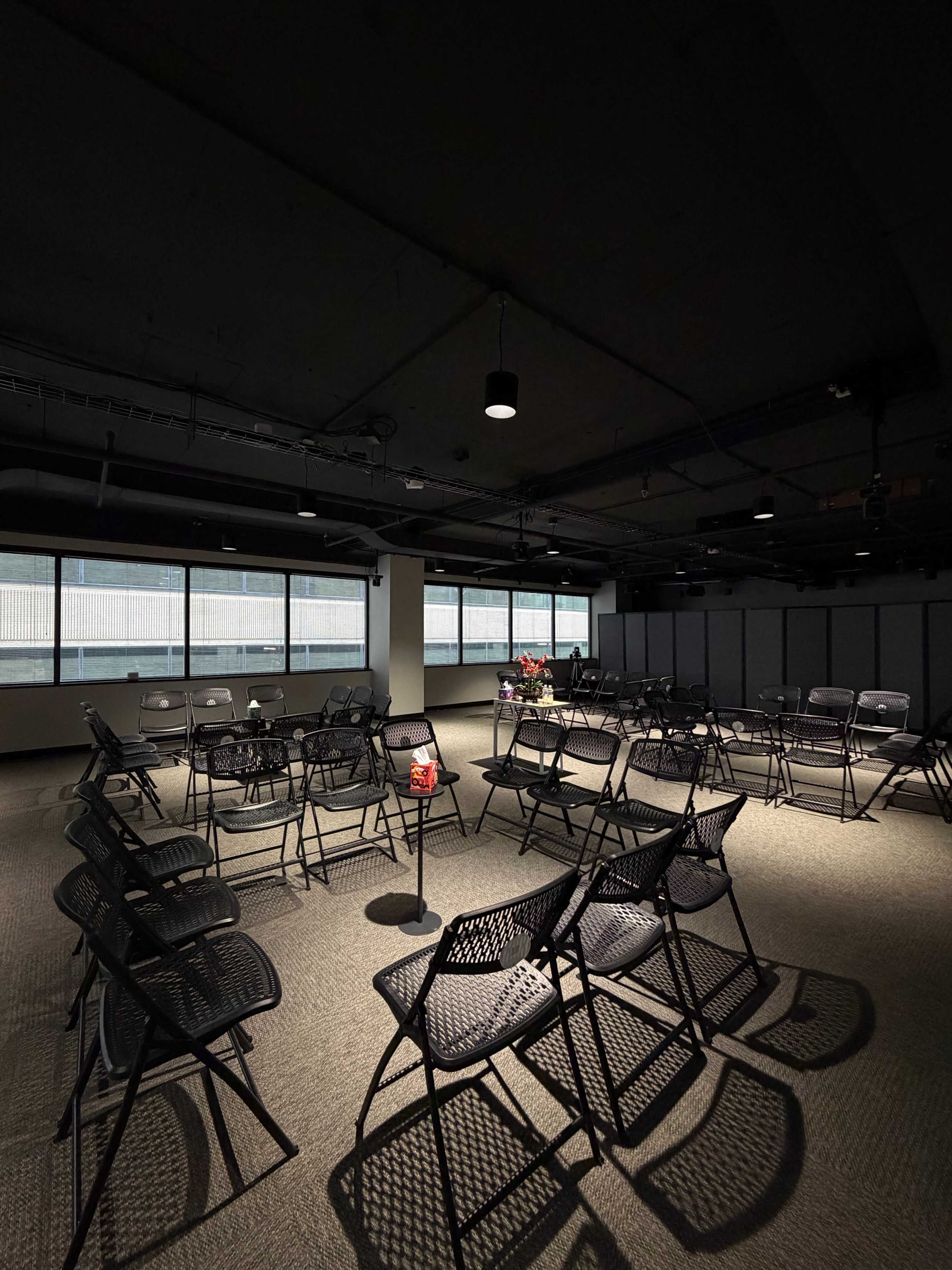 A dimly lit room features several rows of black chairs arranged in a circular formation around a small table.