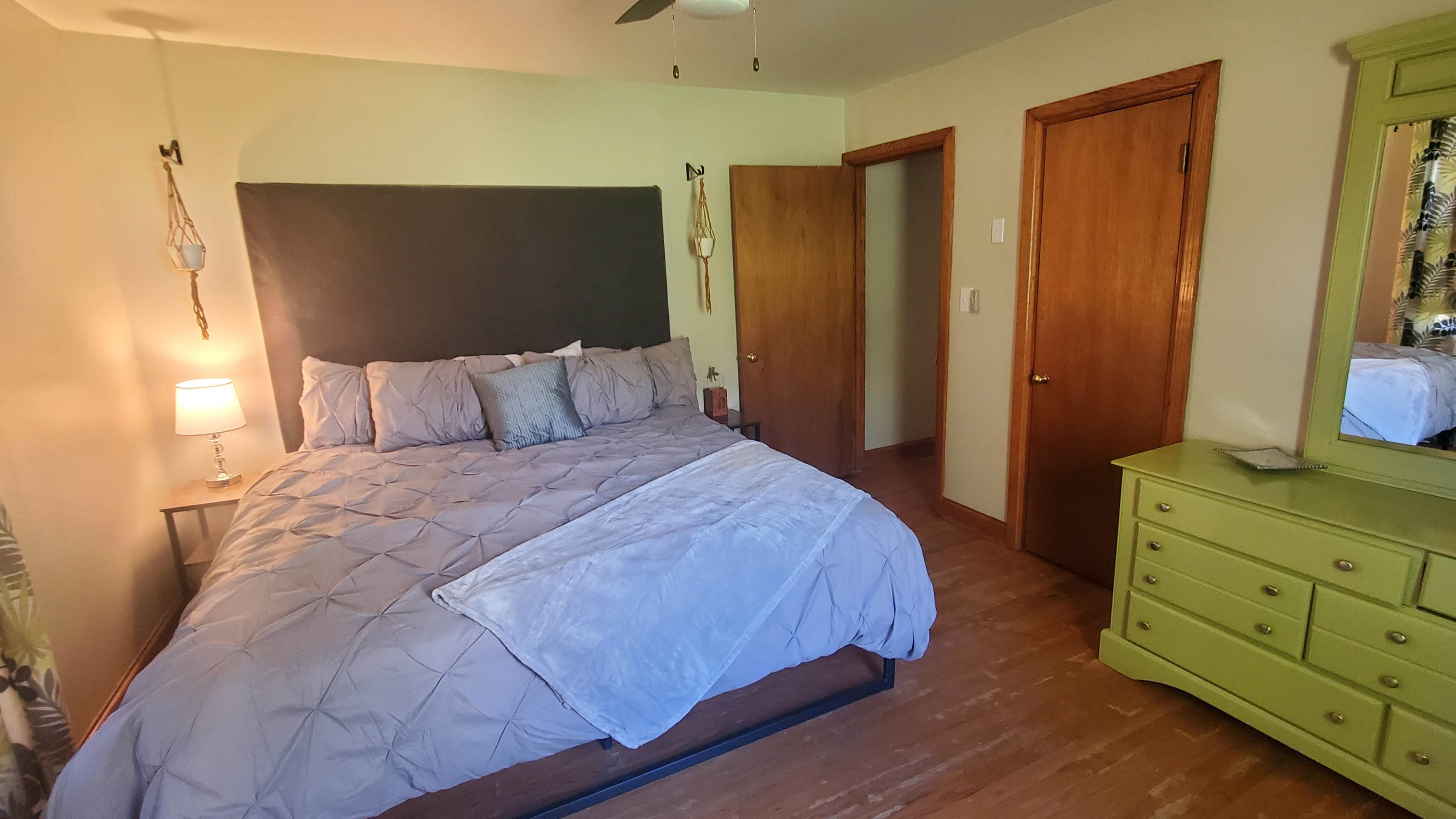 A neatly arranged bedroom features a bed with gray bedding, a bedside lamp, a dresser, and wooden doors.