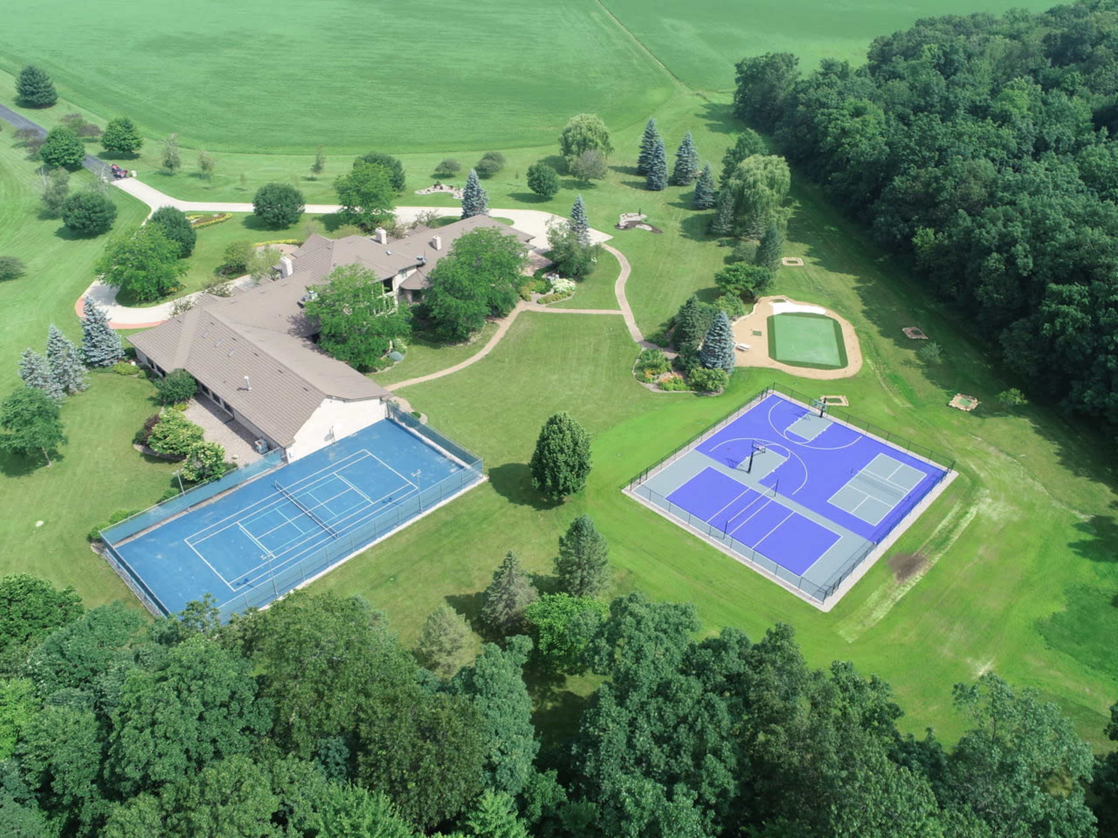 The image shows a large property featuring two tennis courts, a house, a swimming pool, and extensive green grass and trees.