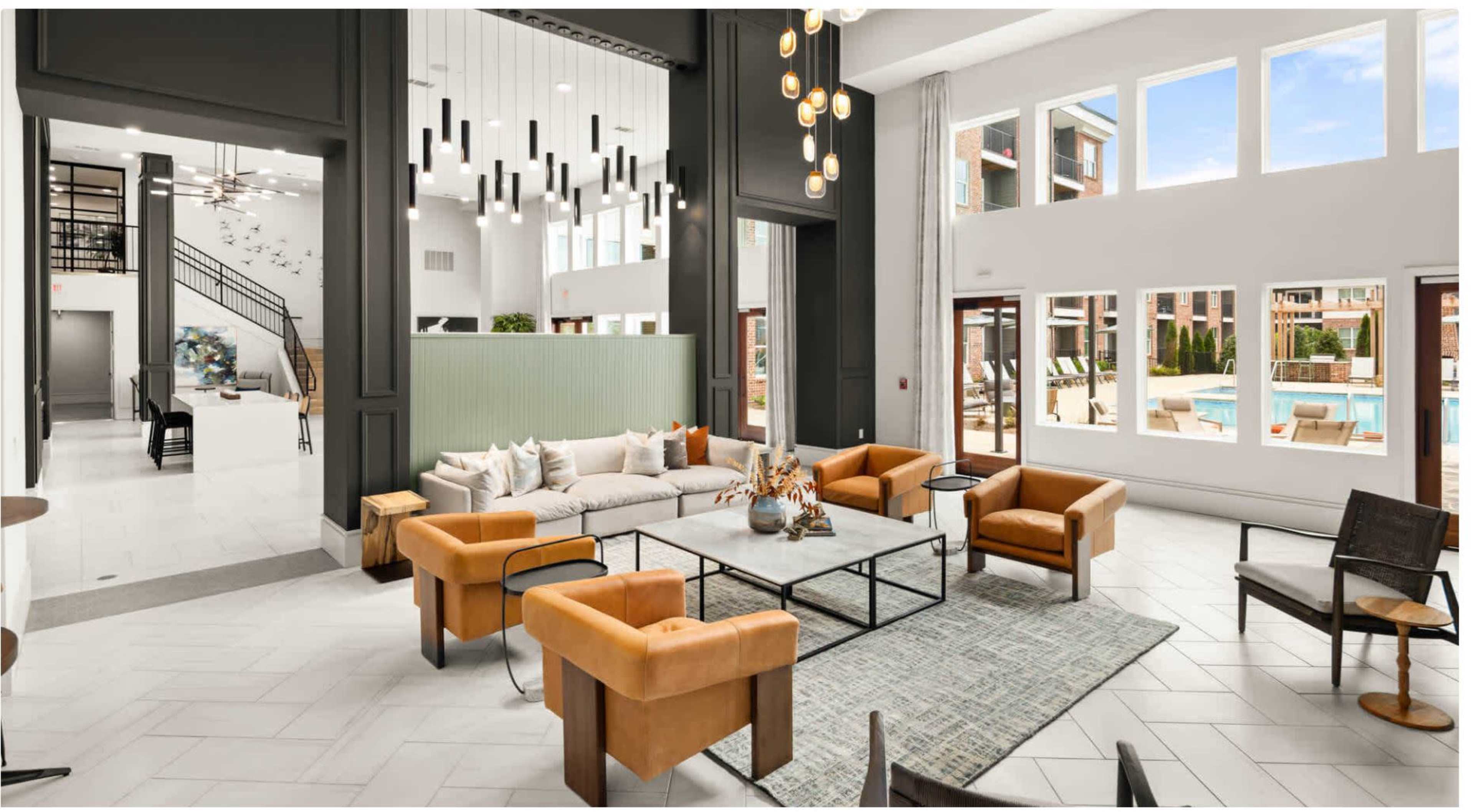 The image shows a modern, spacious lobby area featuring orange armchairs, a large coffee table, and panoramic windows overlooking a pool area.