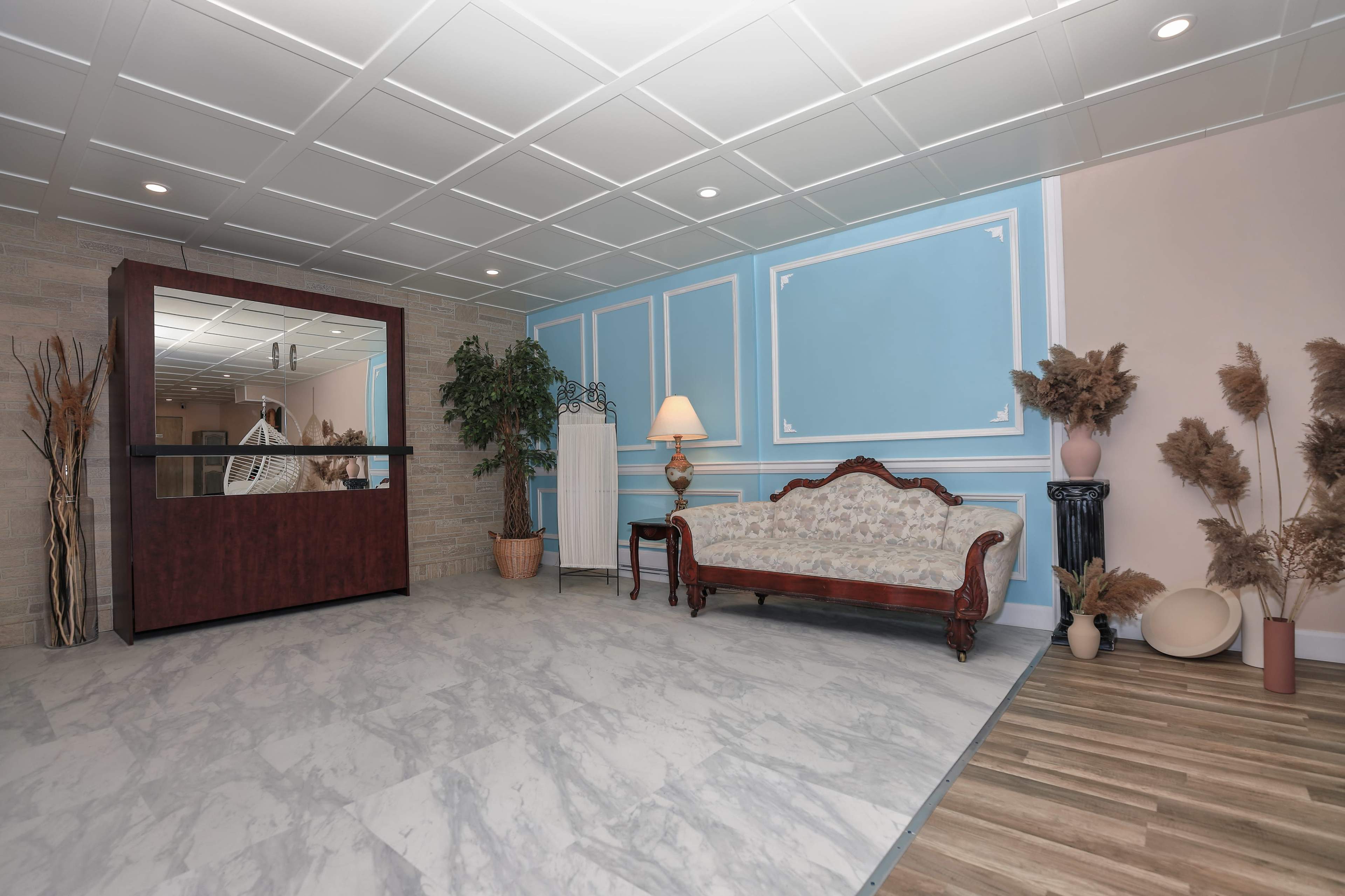 A spacious room with a patterned marble floor, a wooden reception area, a plush couch, and decorative plants against light-colored walls.