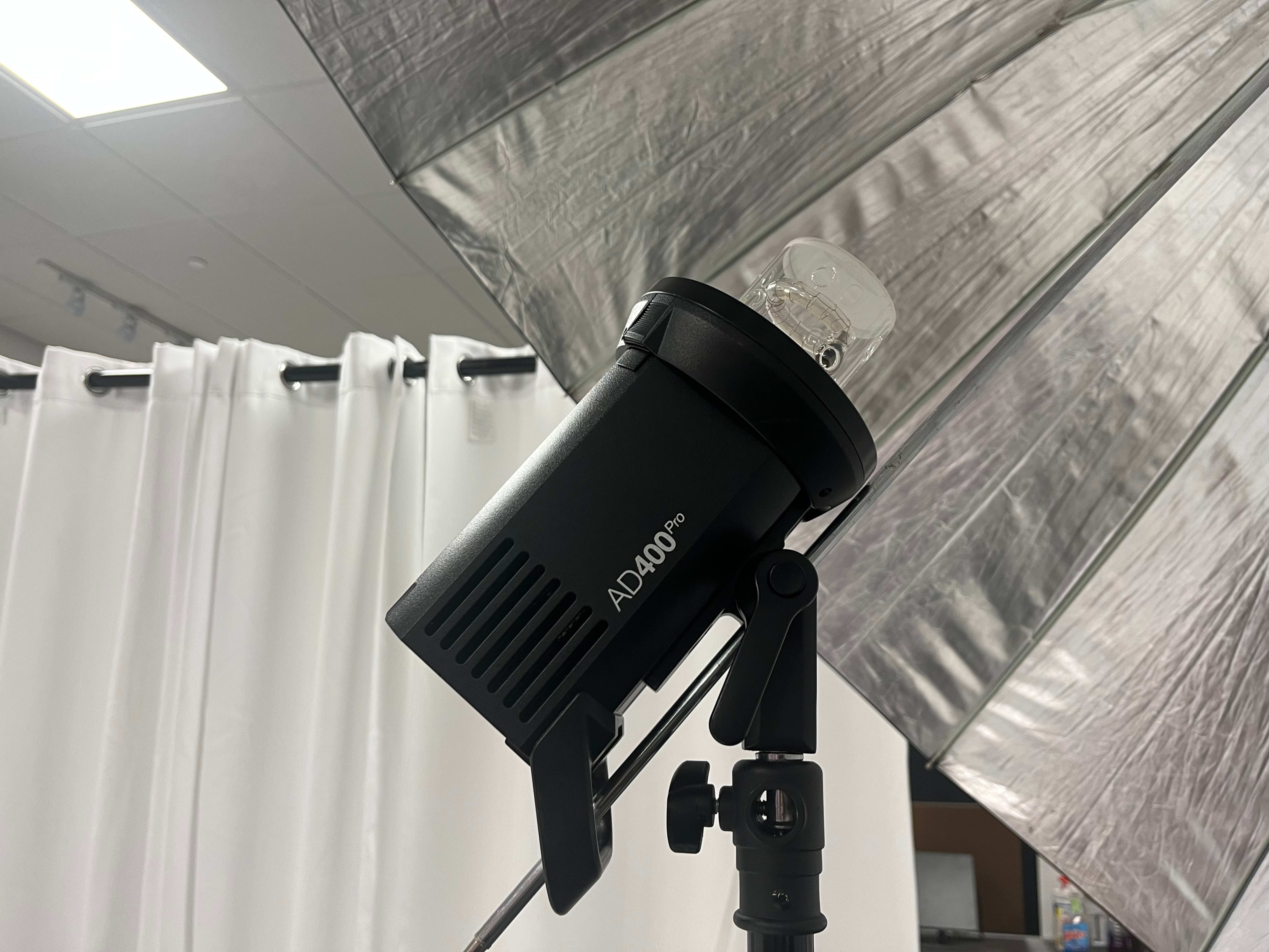 A studio light is mounted on a stand with an umbrella reflector in the background.