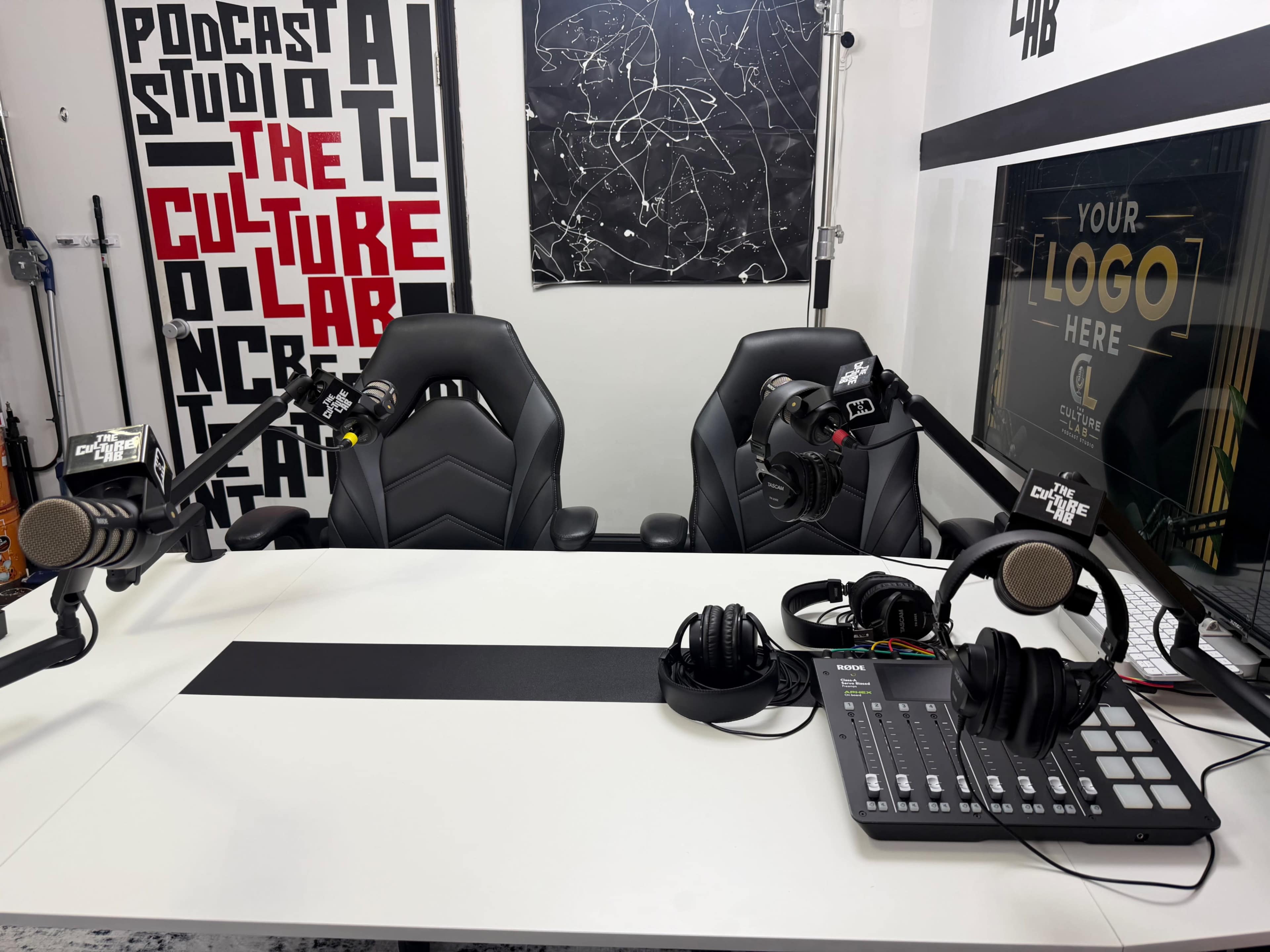 The image shows a modern podcast studio equipped with two black chairs, microphones, headphones, and a digital mixing console on a white table, with a creatively designed backdrop featuring the words "The Culture Lab."