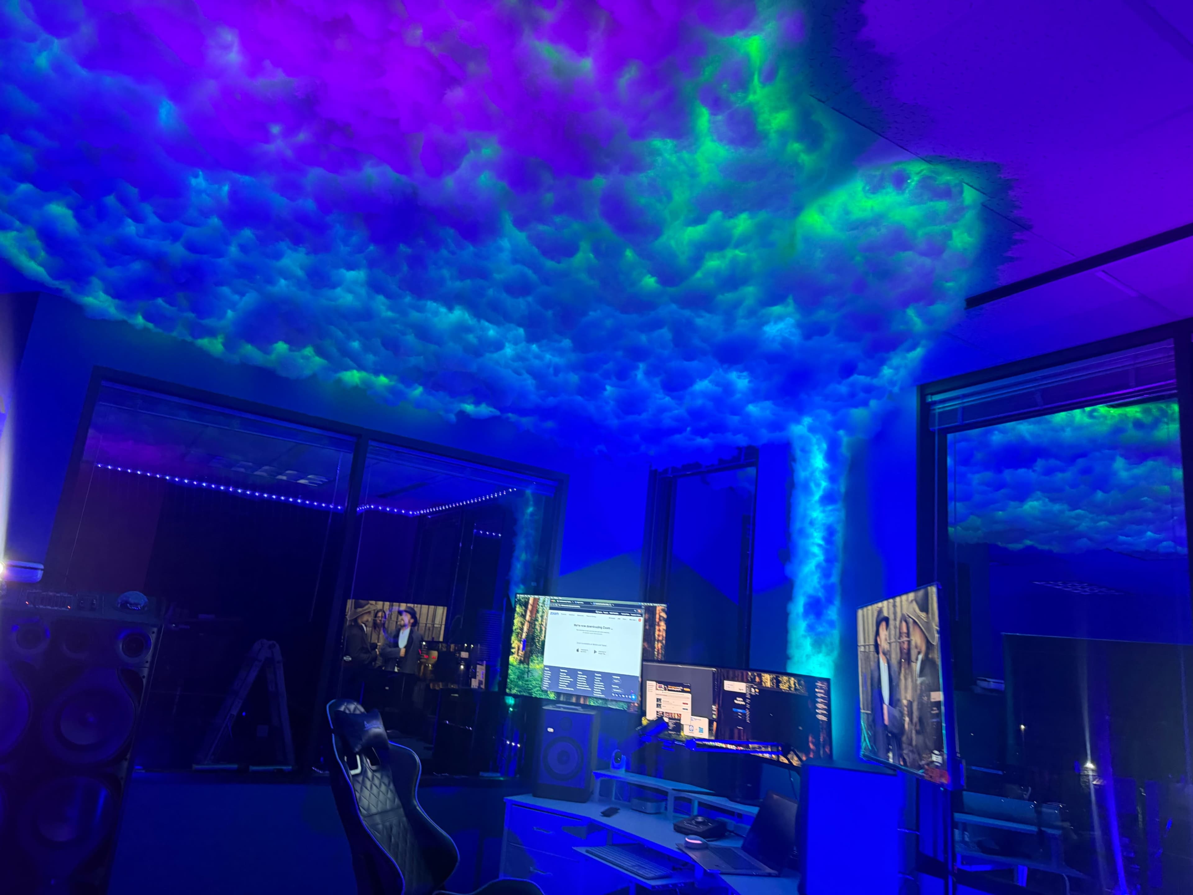 The image shows a modern room with multiple computer monitors and a ceiling illuminated by colorful, cloud-like lighting effects.