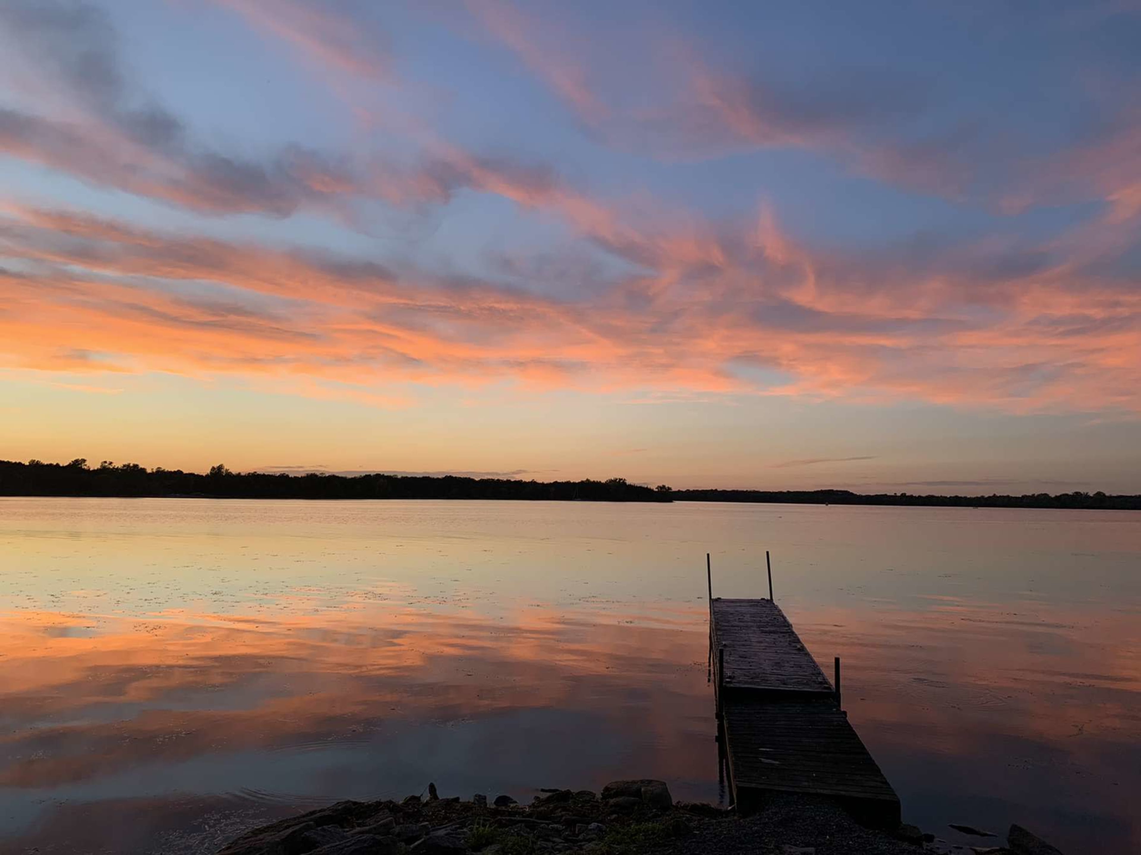 A wooden dock extends into a calm lake under a colorful sunset.