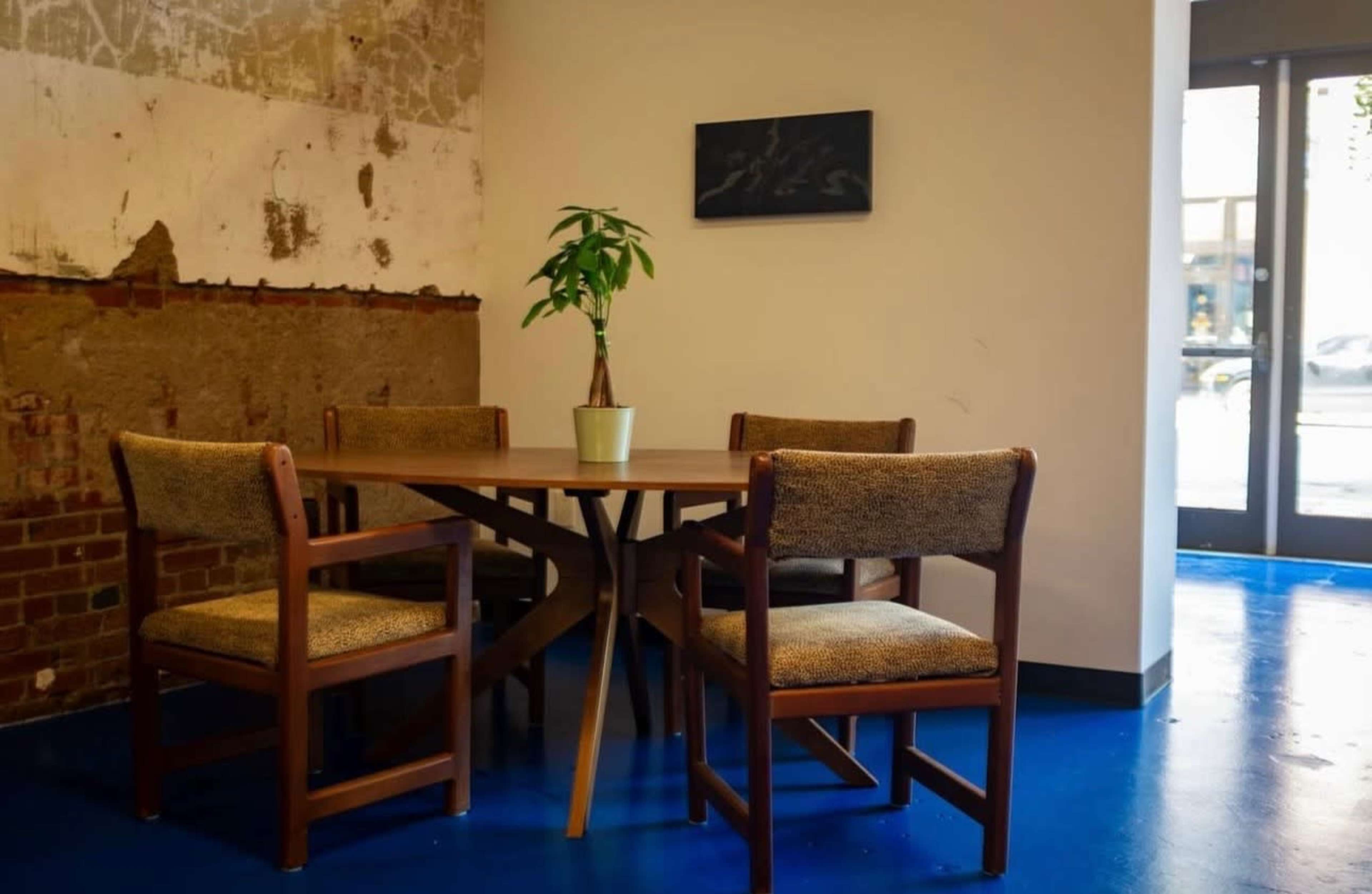 A round wooden table with four chairs is situated in a room with a concrete wall and blue flooring.