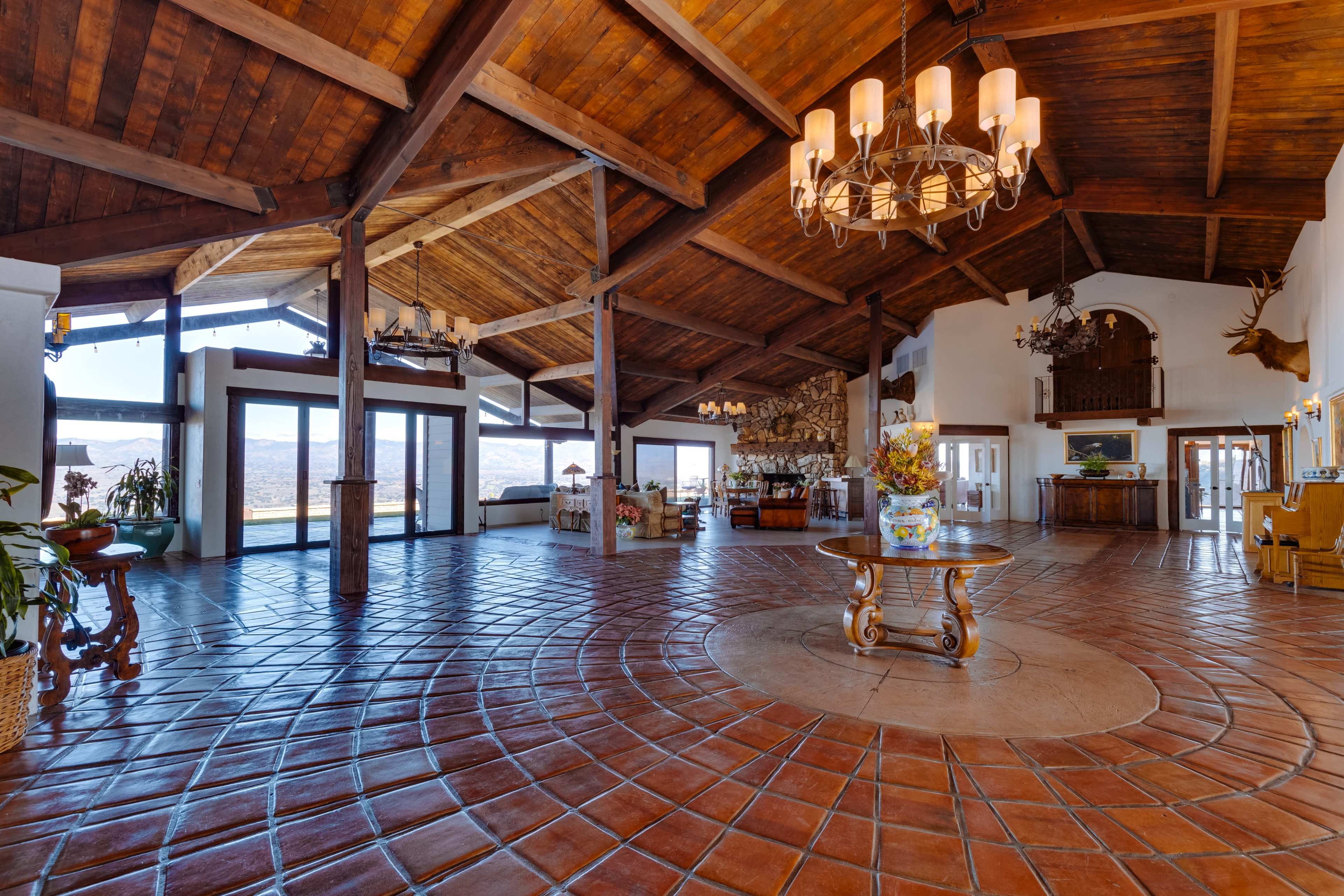 The image depicts a spacious, open interior of a lodge with wooden beams, large windows, and a decorative circular tiled floor.