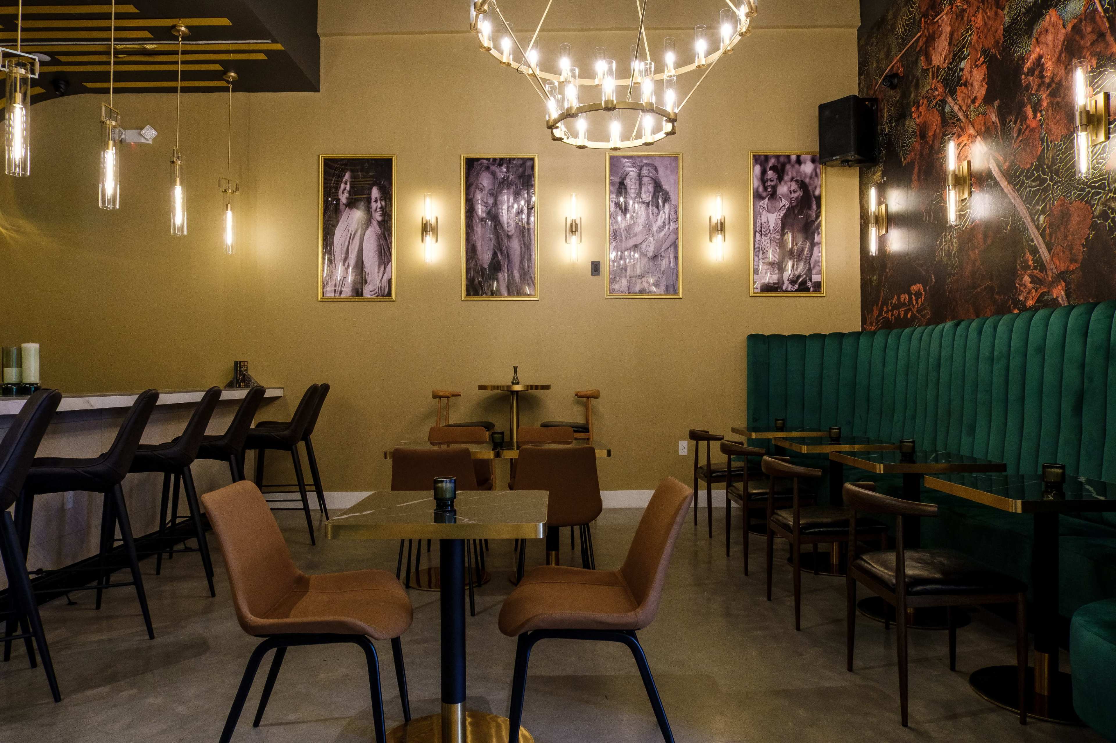 The interior of a modern restaurant features green upholstered seating, a chandelier, and framed black-and-white photographs on the walls.