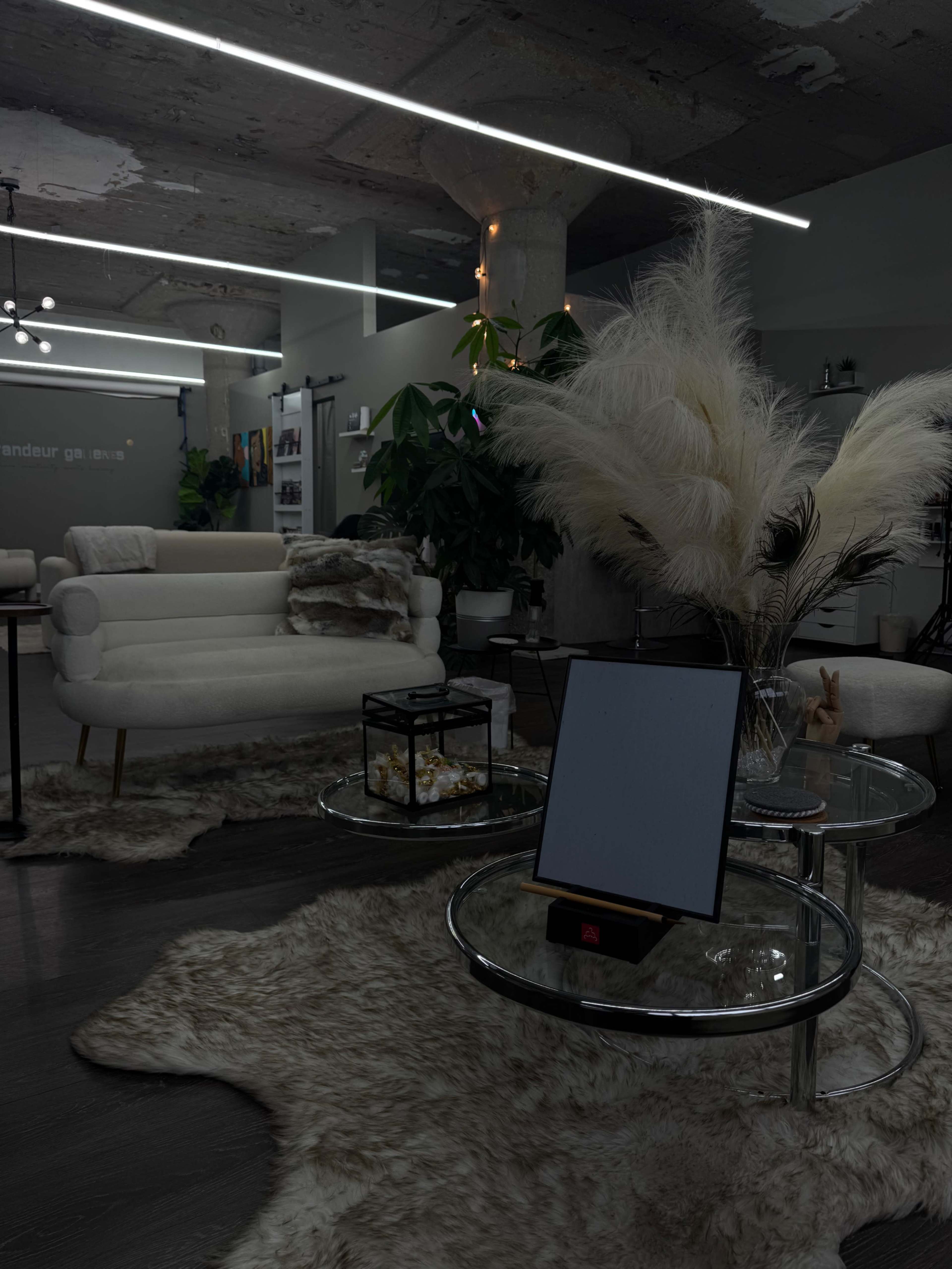 The image shows a modern interior featuring a white sofa, glass coffee tables, decorative plants, and soft rugs under warm lighting.