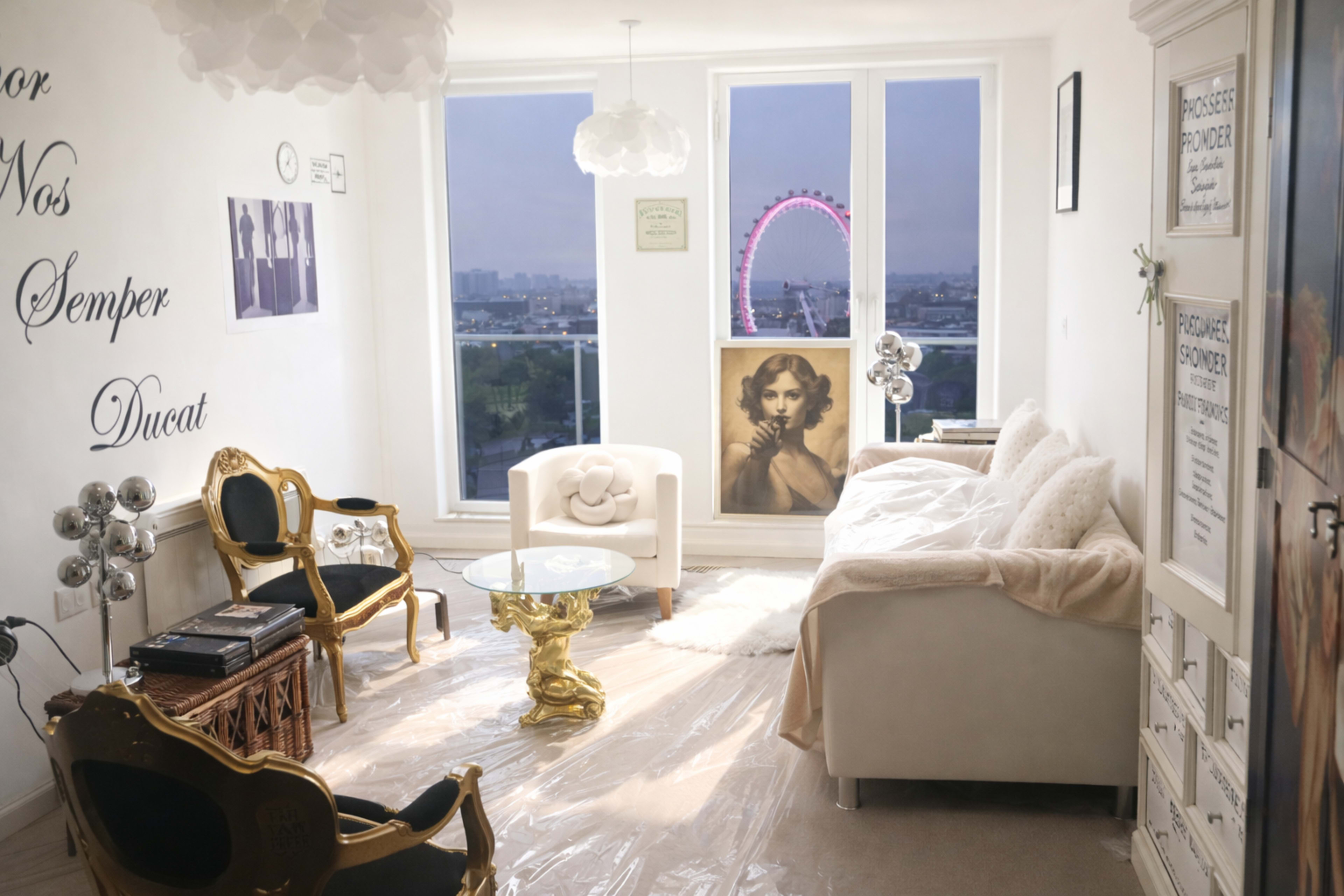 The scene features a modern living room with a white sofa, an ornate gold chair, a glass table, and a large window showcasing the London Eye in the background.