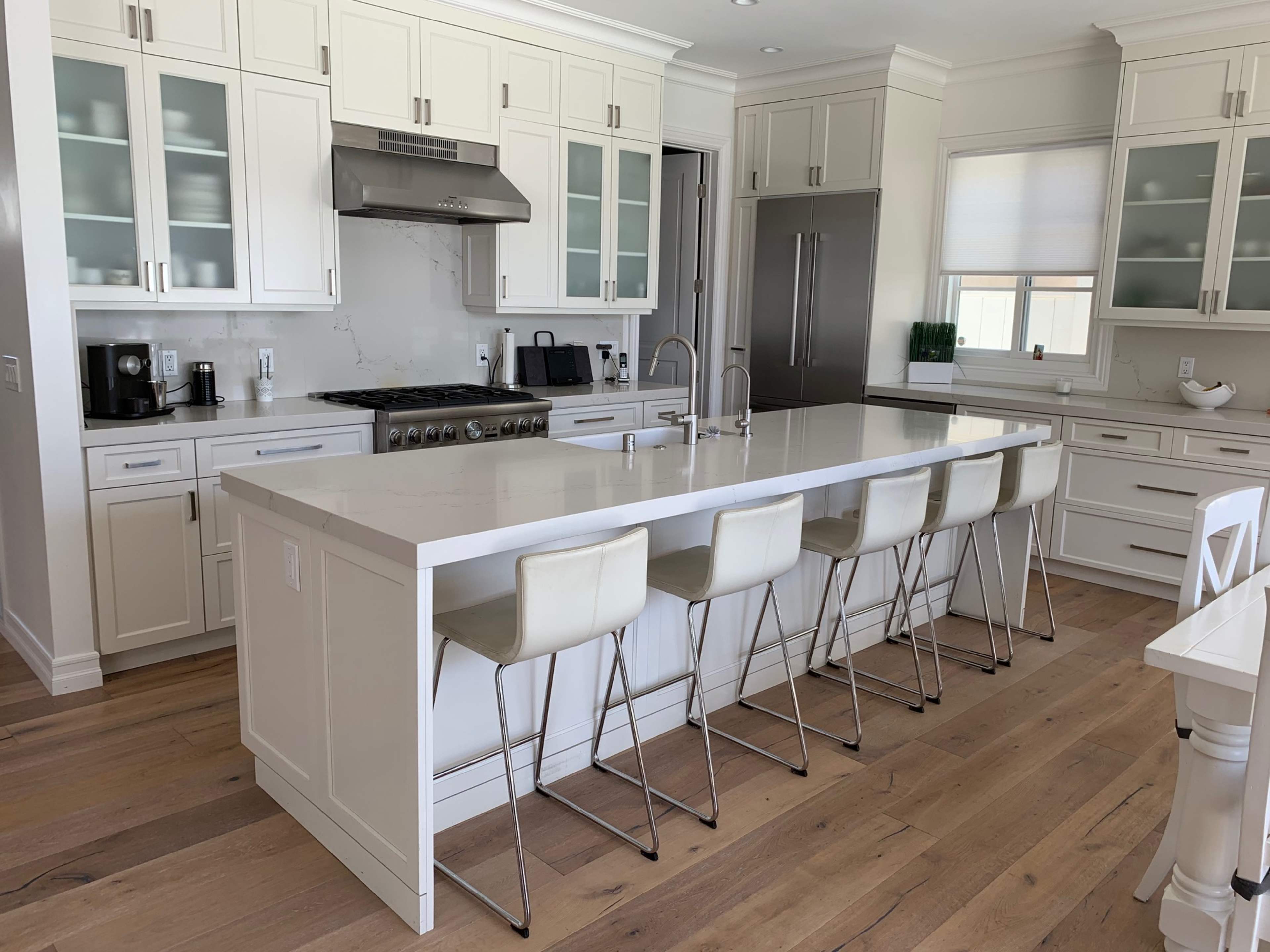 The image shows a modern kitchen with white cabinetry, a large island with seating, and stainless steel appliances.
